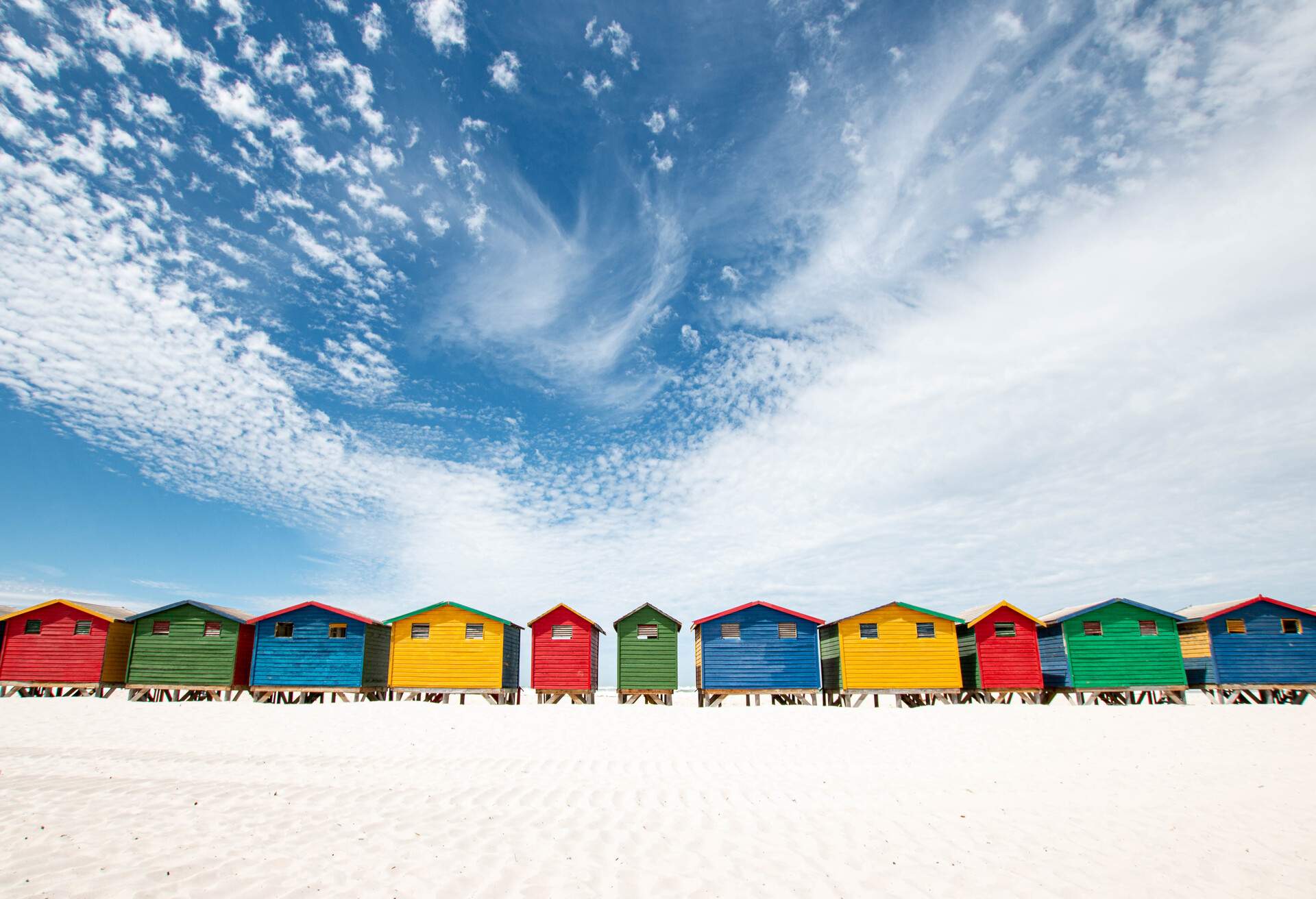 A row of colourful beach huts on a white sand beach under a blue sky.