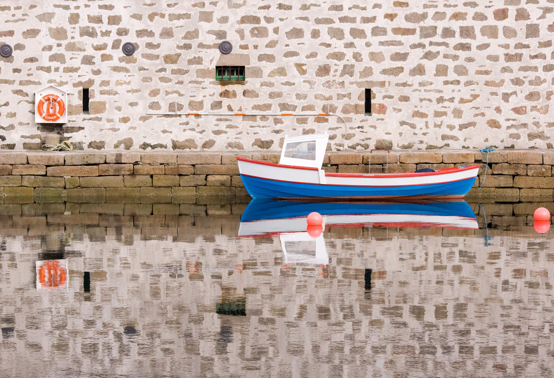 A boat tied to a harbour wall made of sandstone blocks.