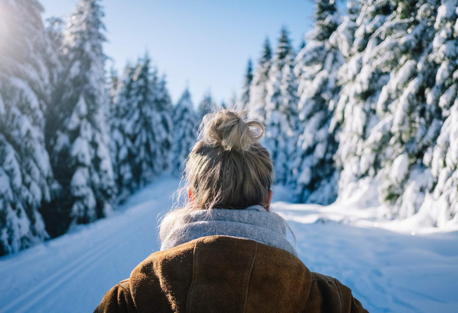 A woman standing on a snow-covered path lined with frosted trees.