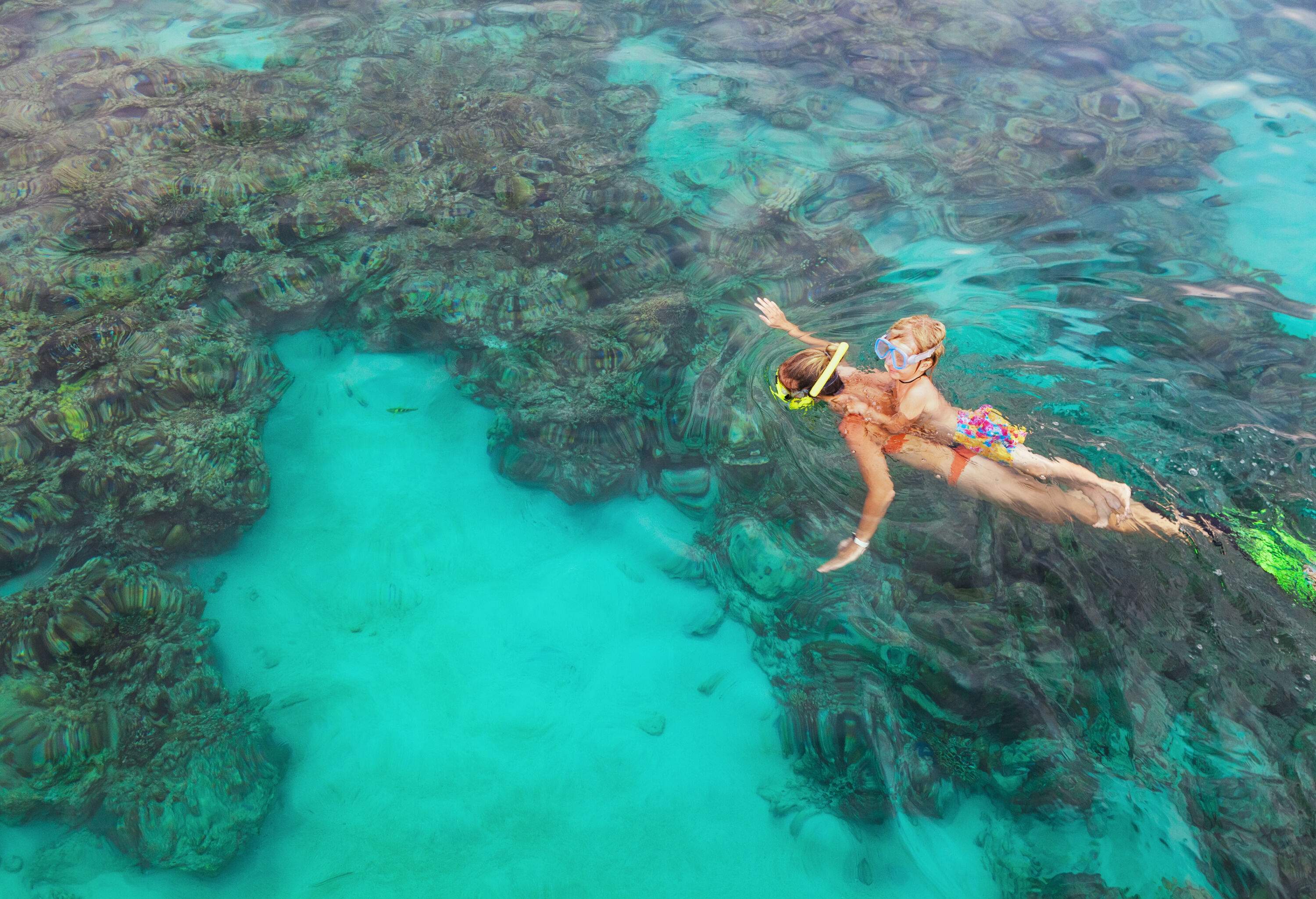 A mother snorkelling with her daughter behind in a coral reef sea pool.