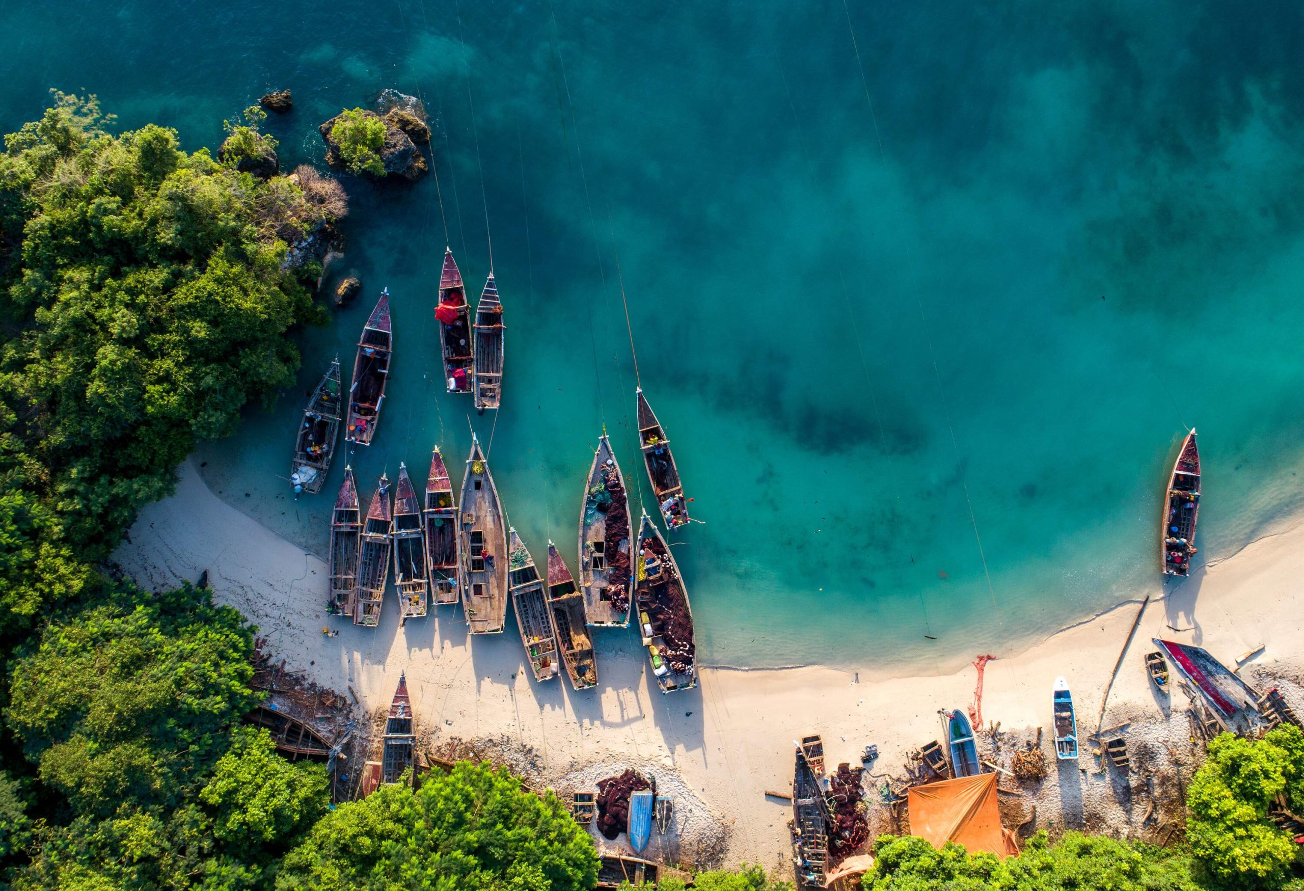 Top view of moored fishing boats on the lush white sand shore of a tranquil beach.