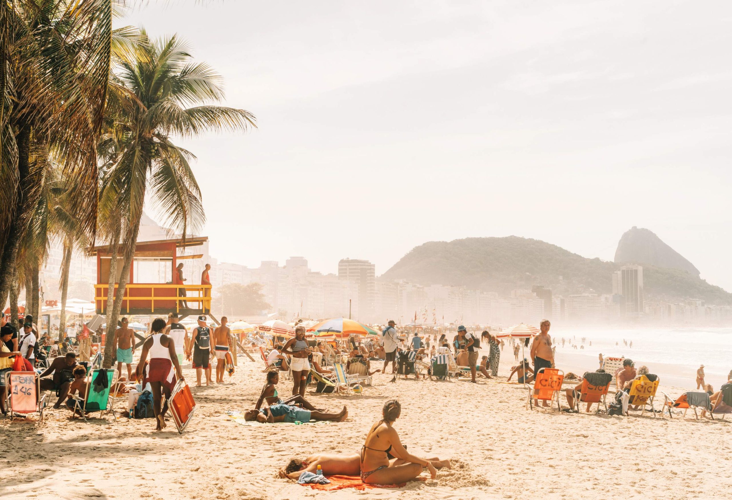 A crowded beach with people relaxing and sunbathing under the sun.