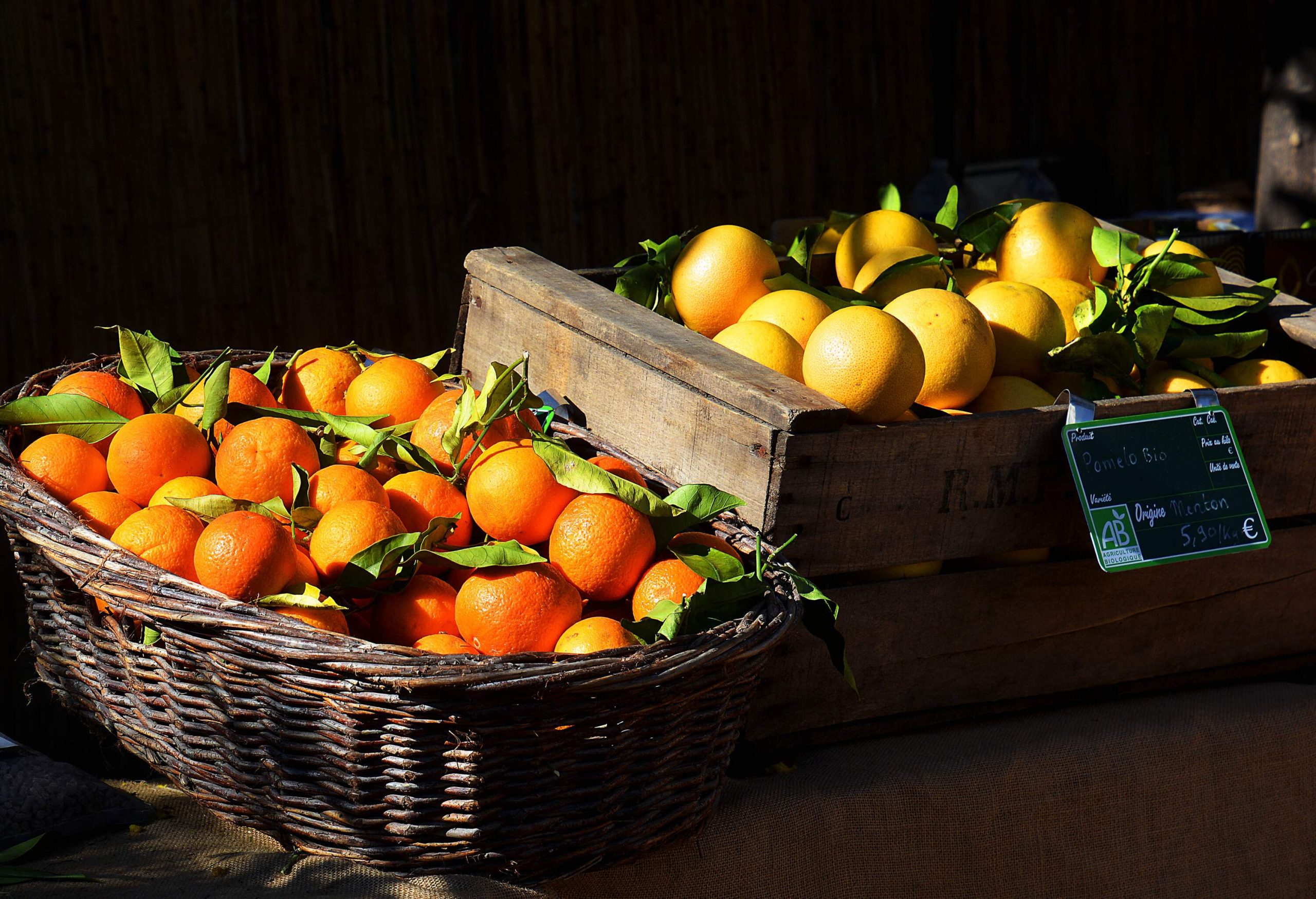A basket full of oranges and a wooden crate filled with lemons on display.