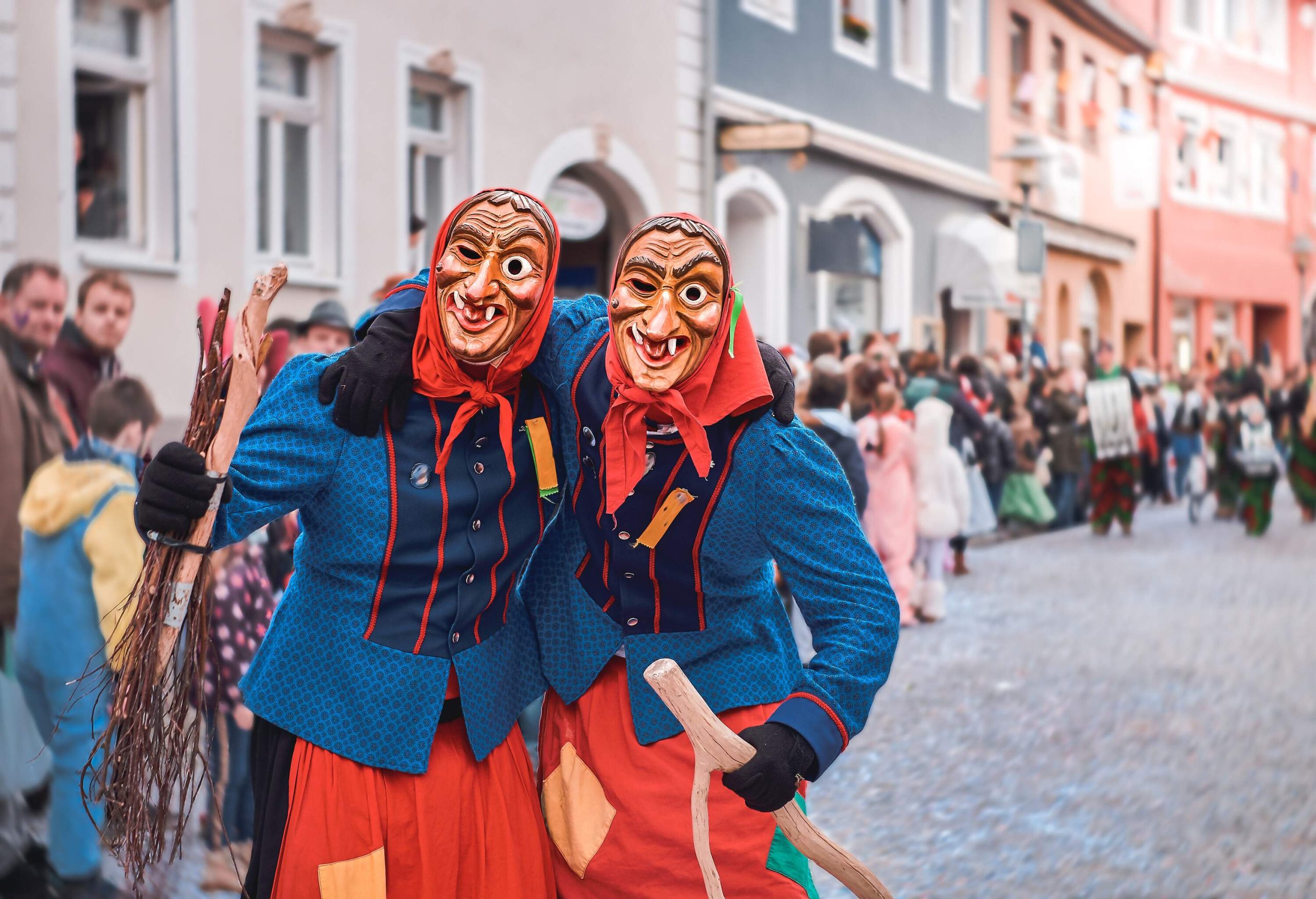 Two individuals in witch costumes with bokeh backgrounds of people against the colourful buildings.