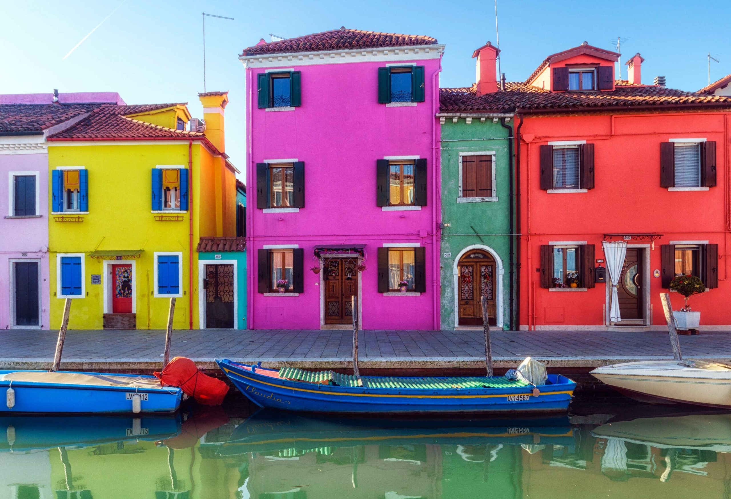 A water canal with anchored boats along a promenade with colourful buildings.