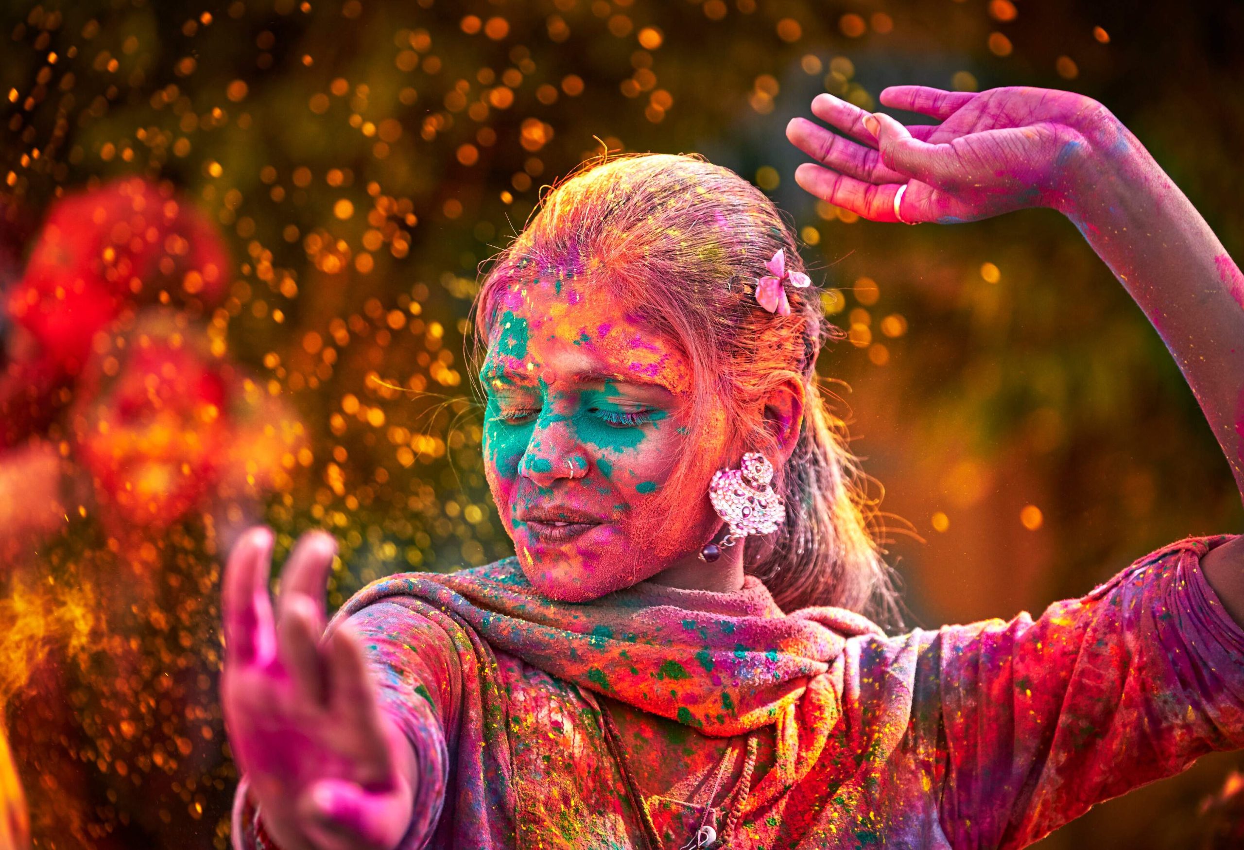 A woman with big earrings dancing after being thrown with colourful dye powder during the Holi festival.