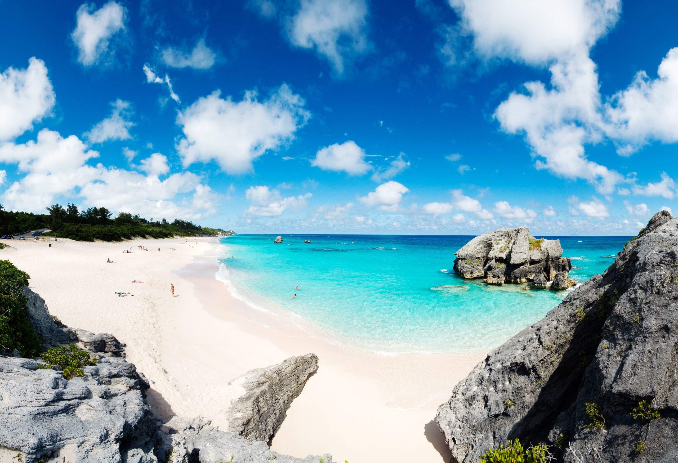 A pristine sandy beach with turquoise seas beneath a deep blue daytime sky with patches of white clouds.