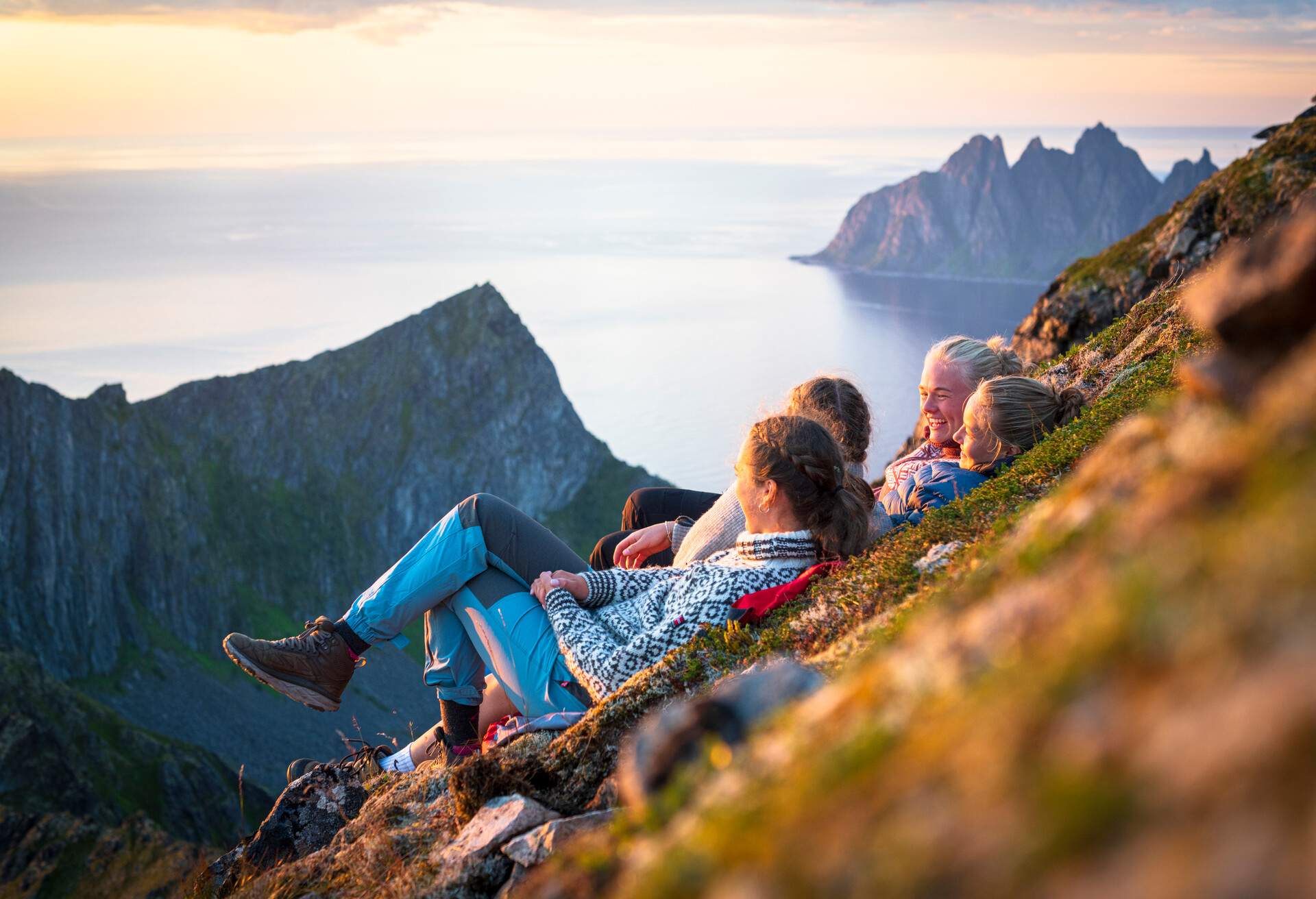 Scandinavian girls having fun lying on mountain ridge at sunset, Senja island, Troms county, Norway