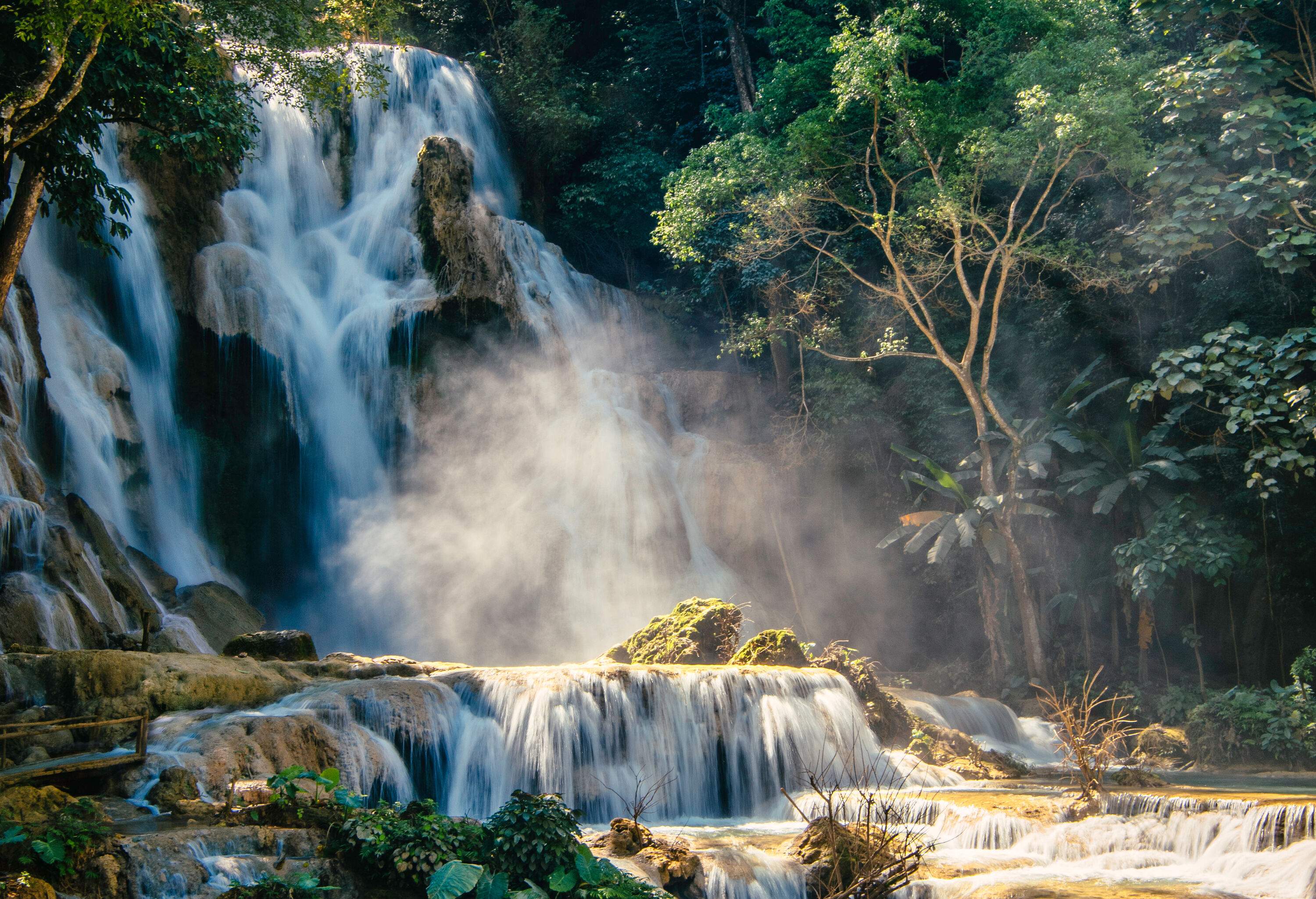 A beautiful waterfall cascades into the tiered rocky streams surrounded by lush trees.