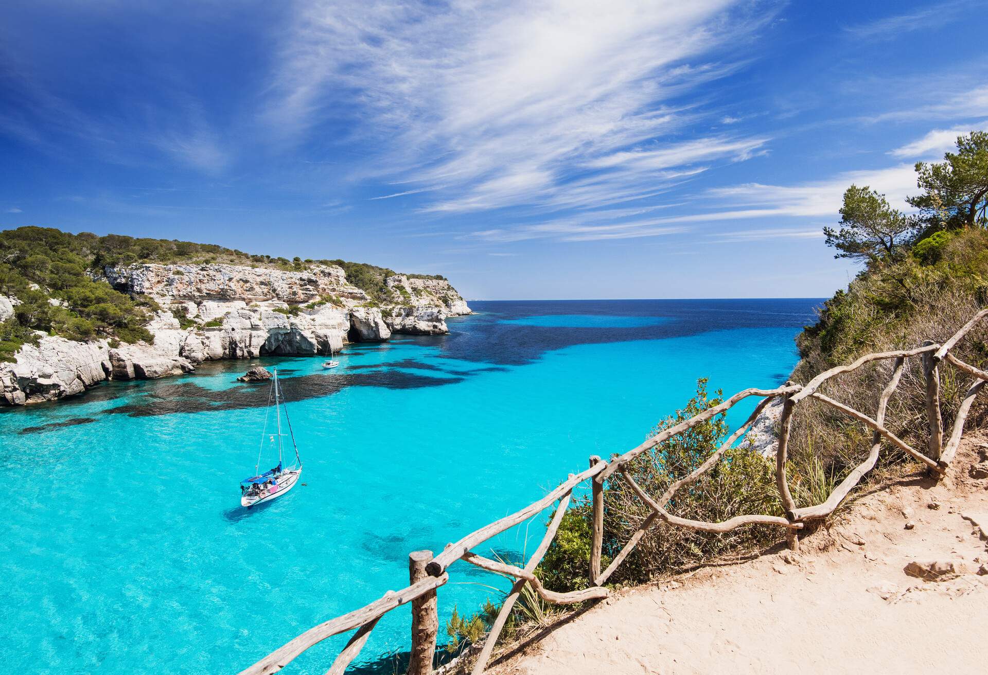 A boat sailing in a turquoise-watered bay surrounded by forested limestone cliffs.