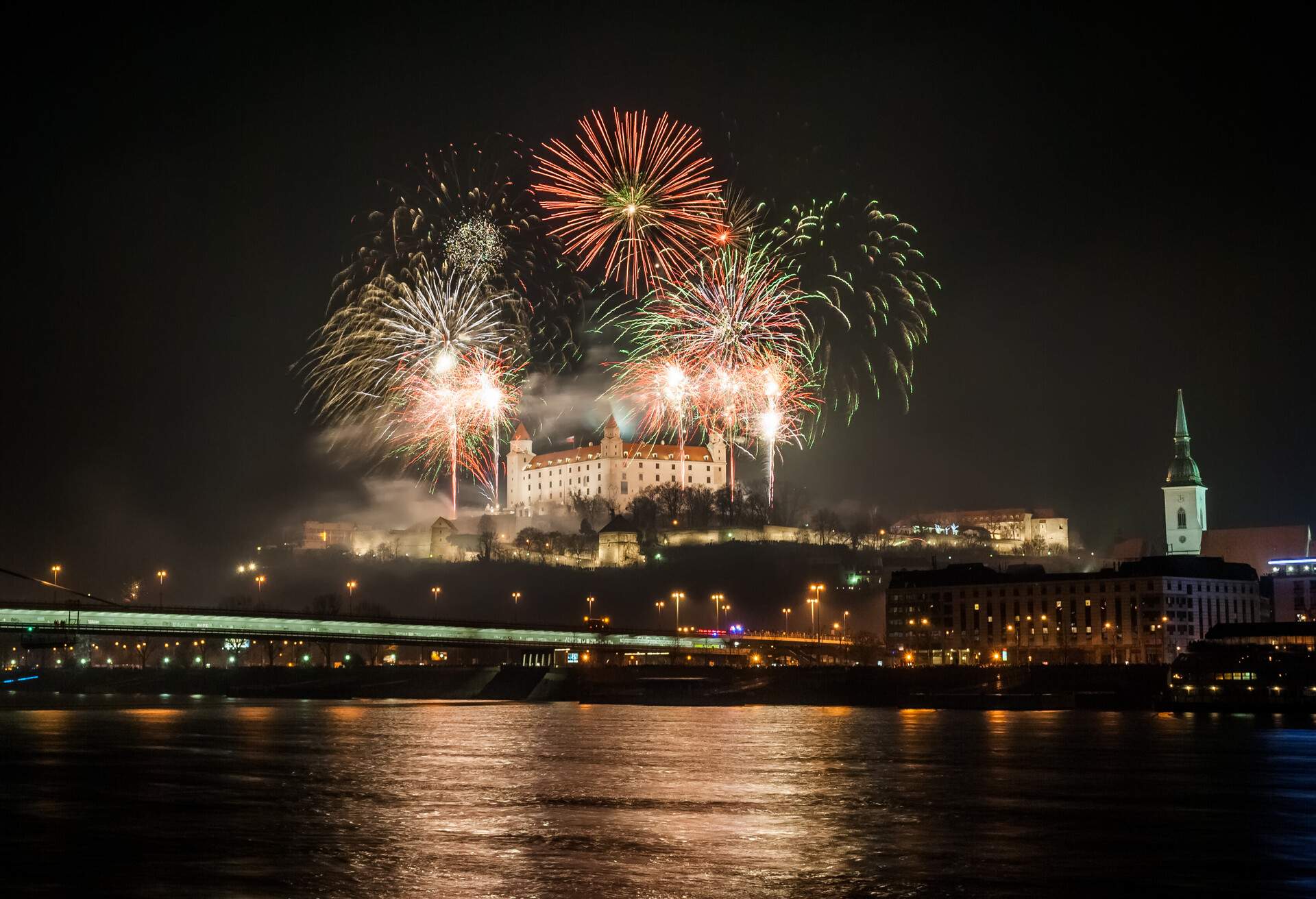 Bright fireworks across the river offer a magnificent show against the urban backdrop as they illuminate Bratislava Castle's outline.