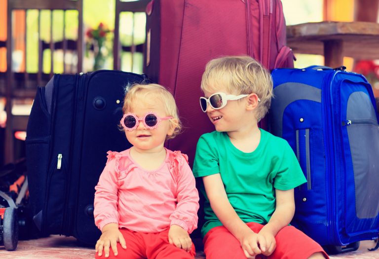 little boy and toddler girl sitting on suitcases ready to travel, kids travel concept