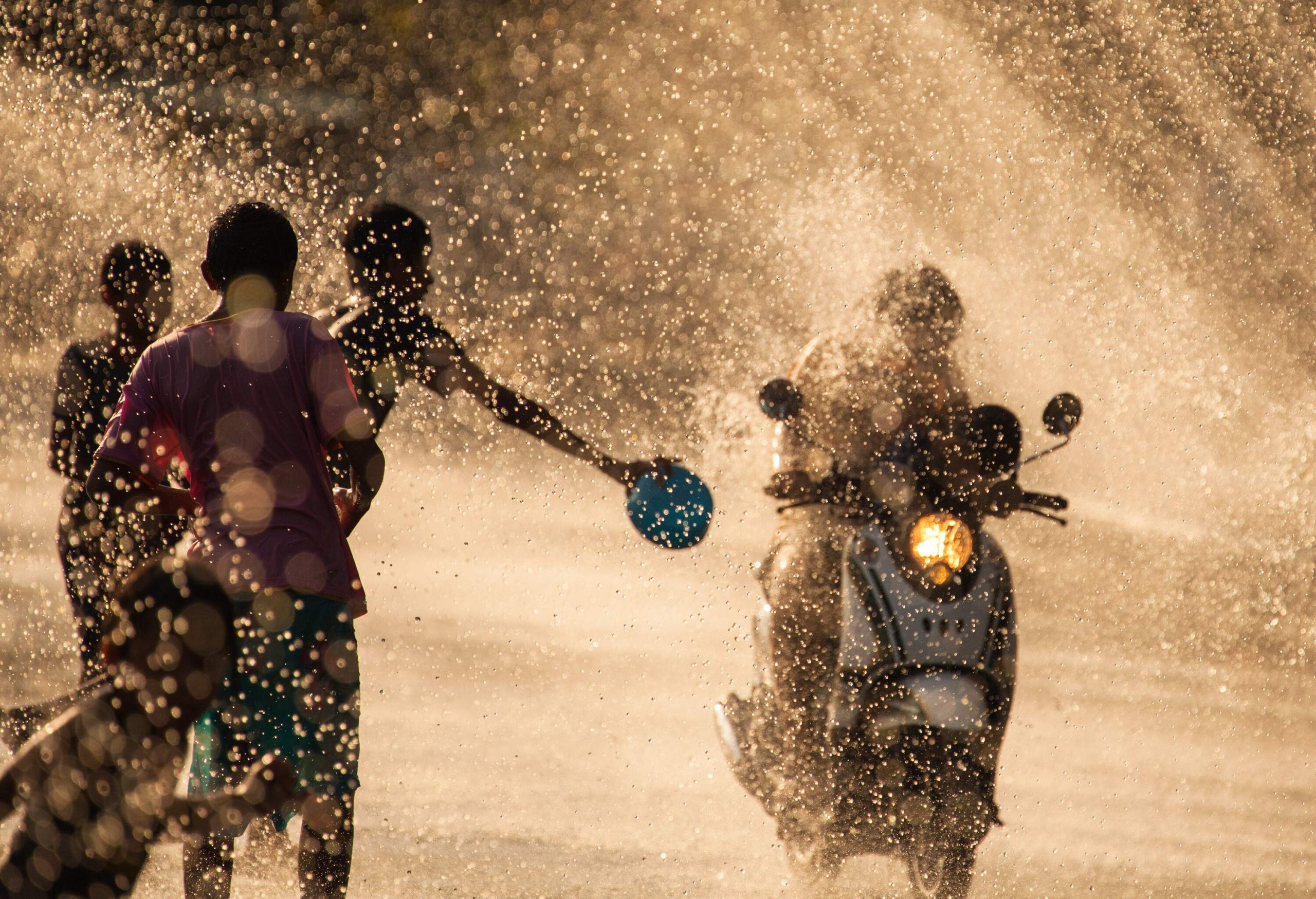 Kids splashing water to a passing motorcycle rider.