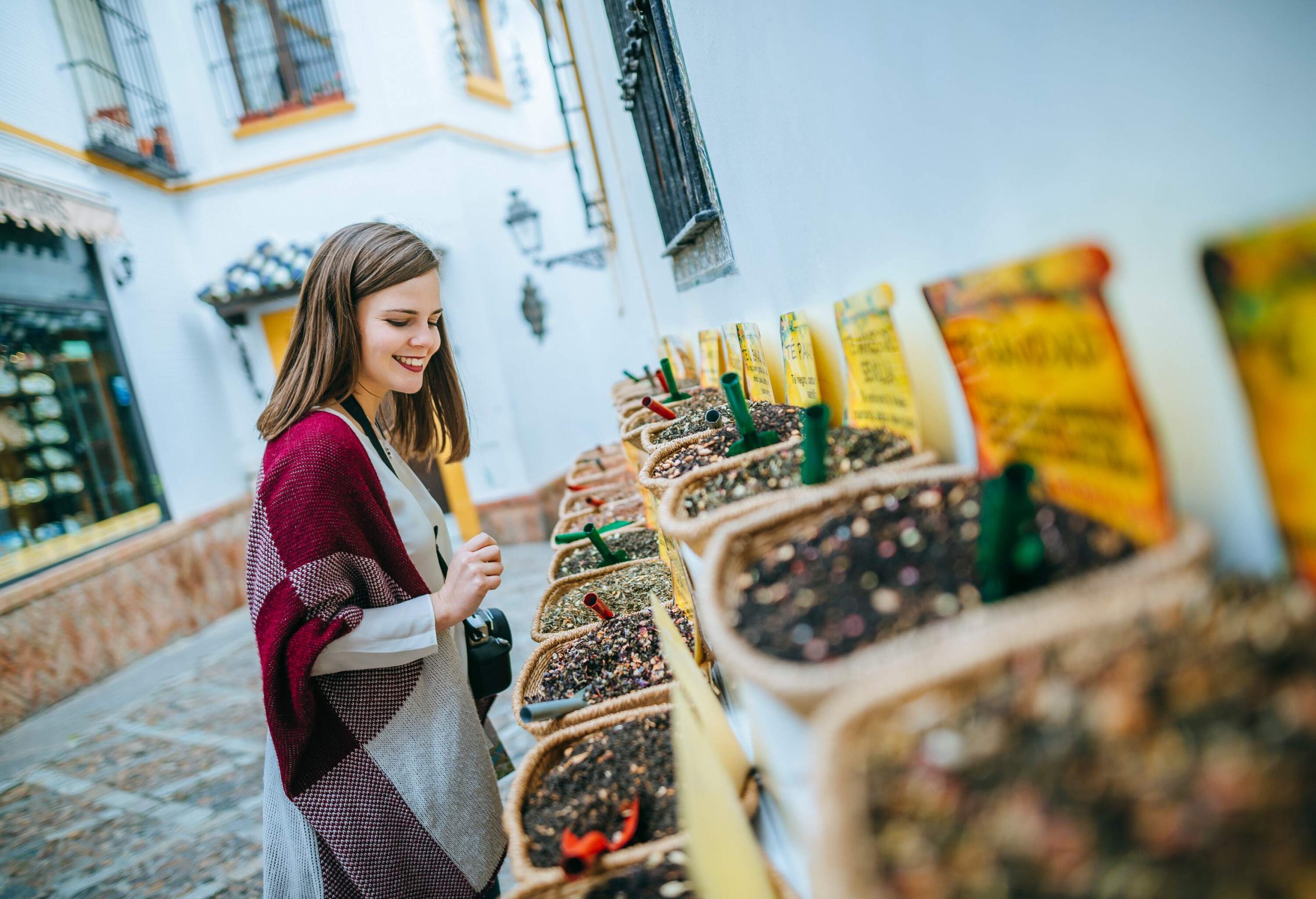 A smiling woman is about to decide what to buy in a spice shop.