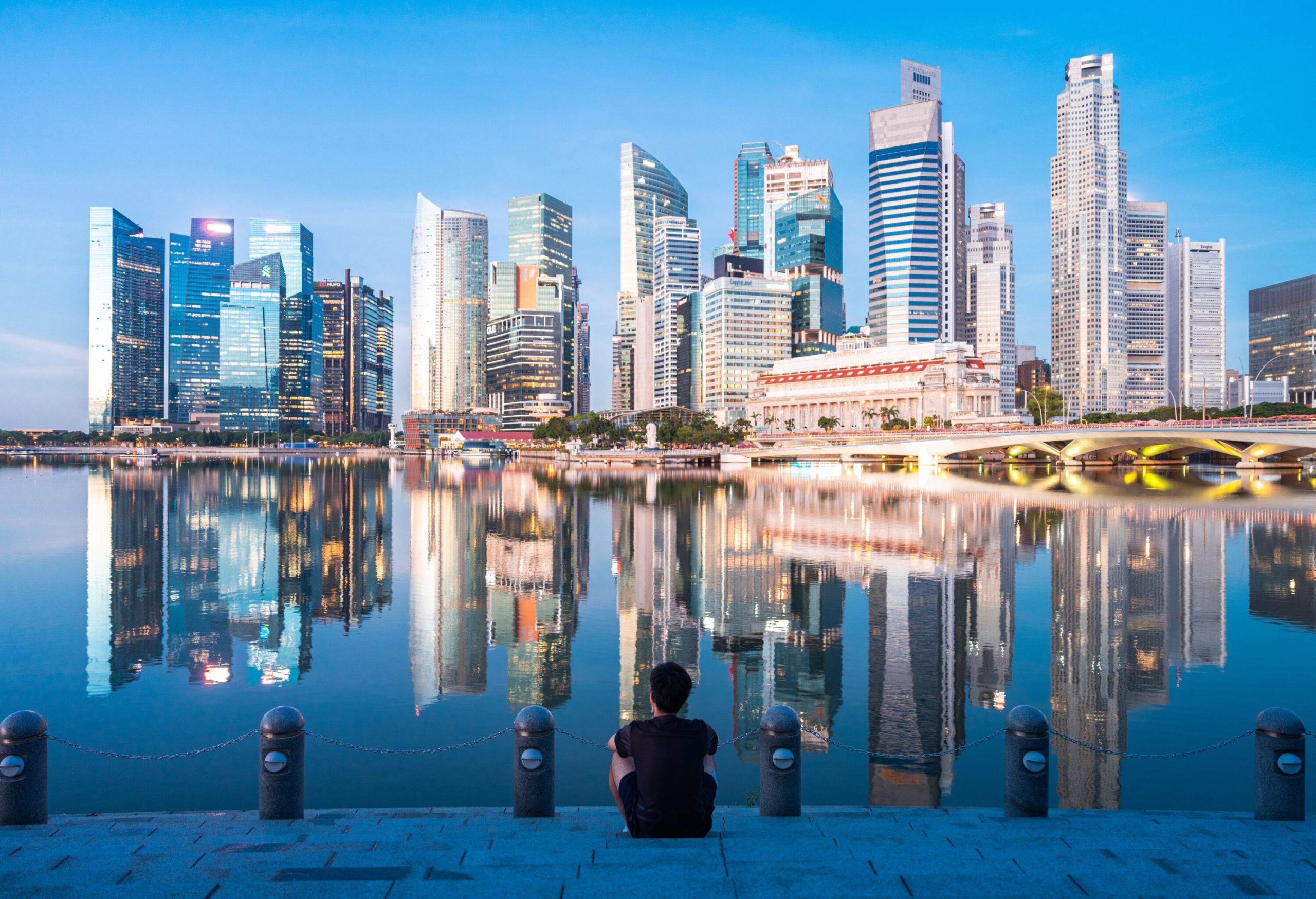 The young man sat and stand on the dock with urban skyline and skyscrapers in Marina Bay Singapore.