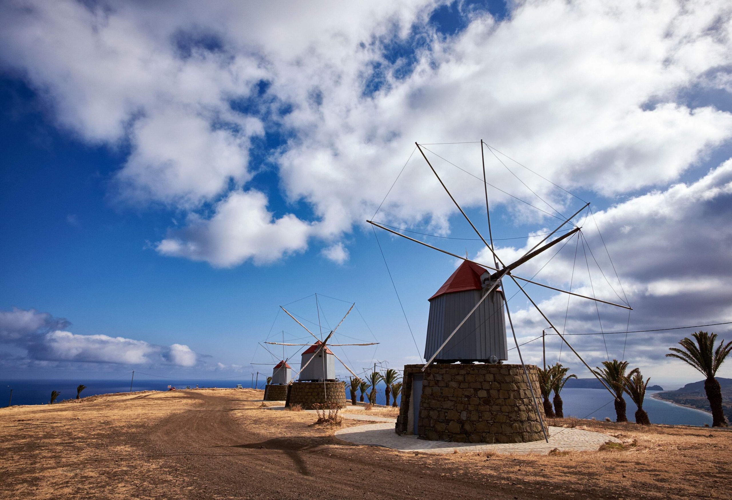 Three traditional hilltop windmills with overlooking views of a vast ocean.