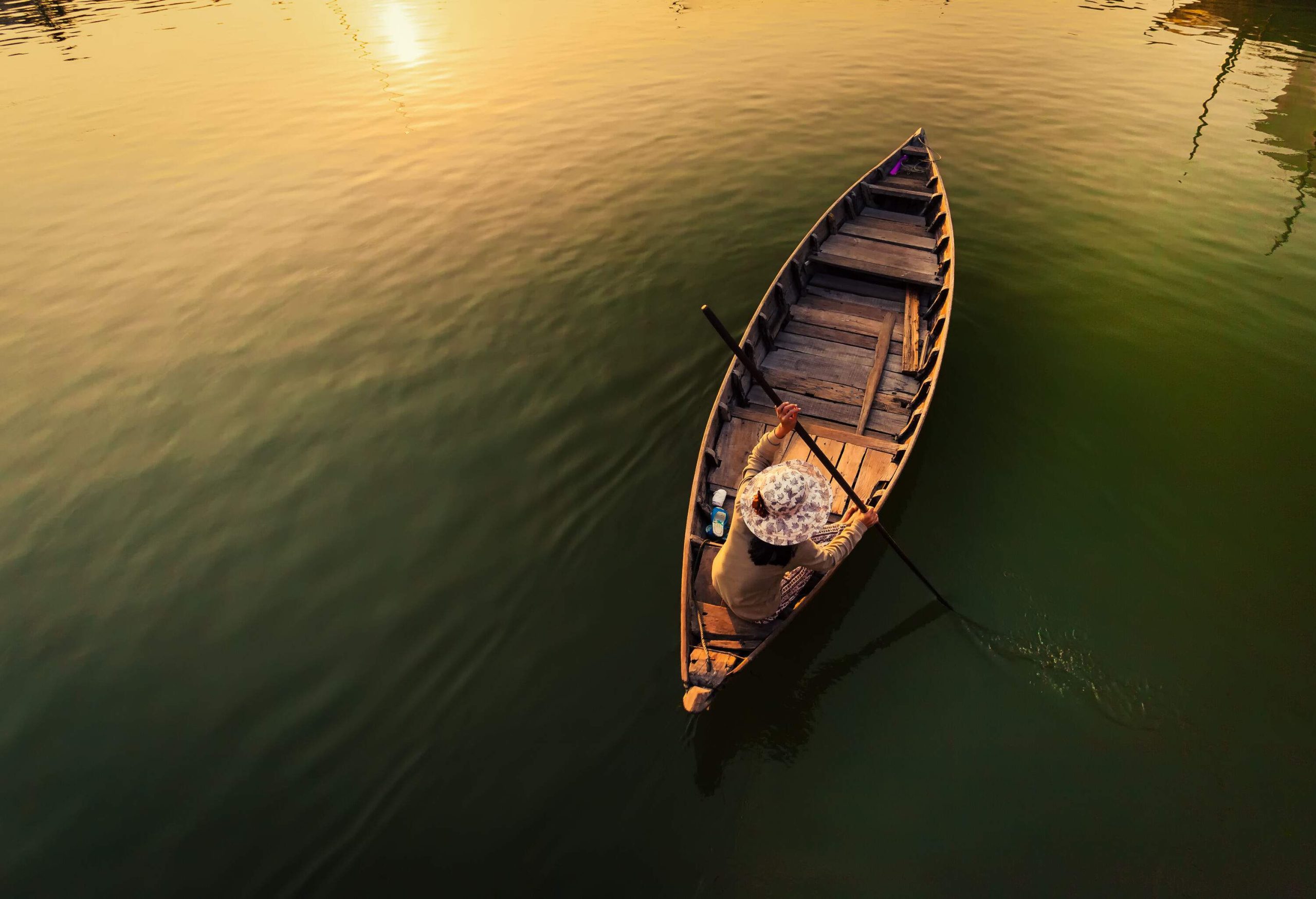 An individual on a wooden boat, paddling on tranquil waters at twilight.