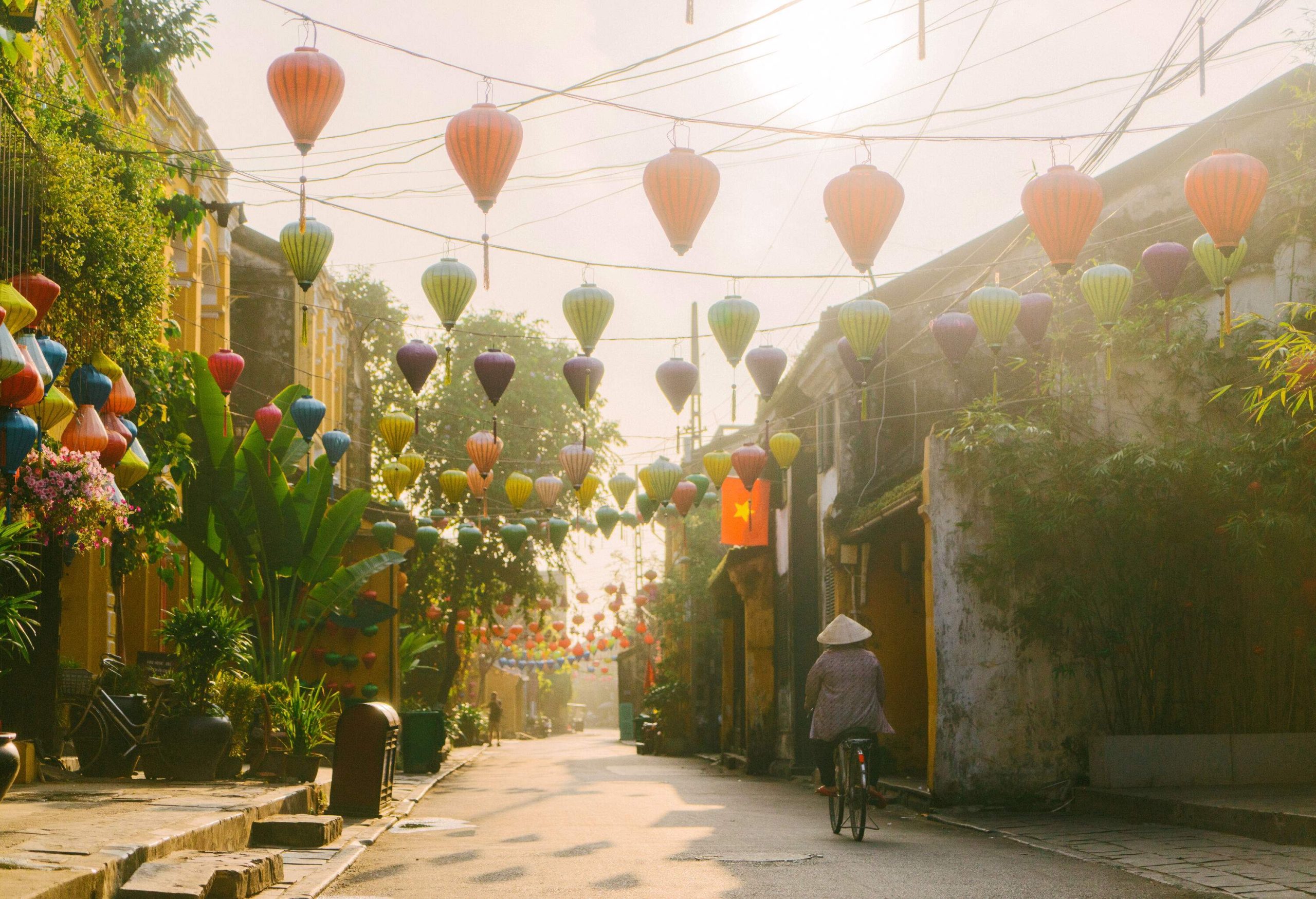 An individual on a bicycle along a paved street, surrounded by charming classic houses adorned with hanging lanterns.