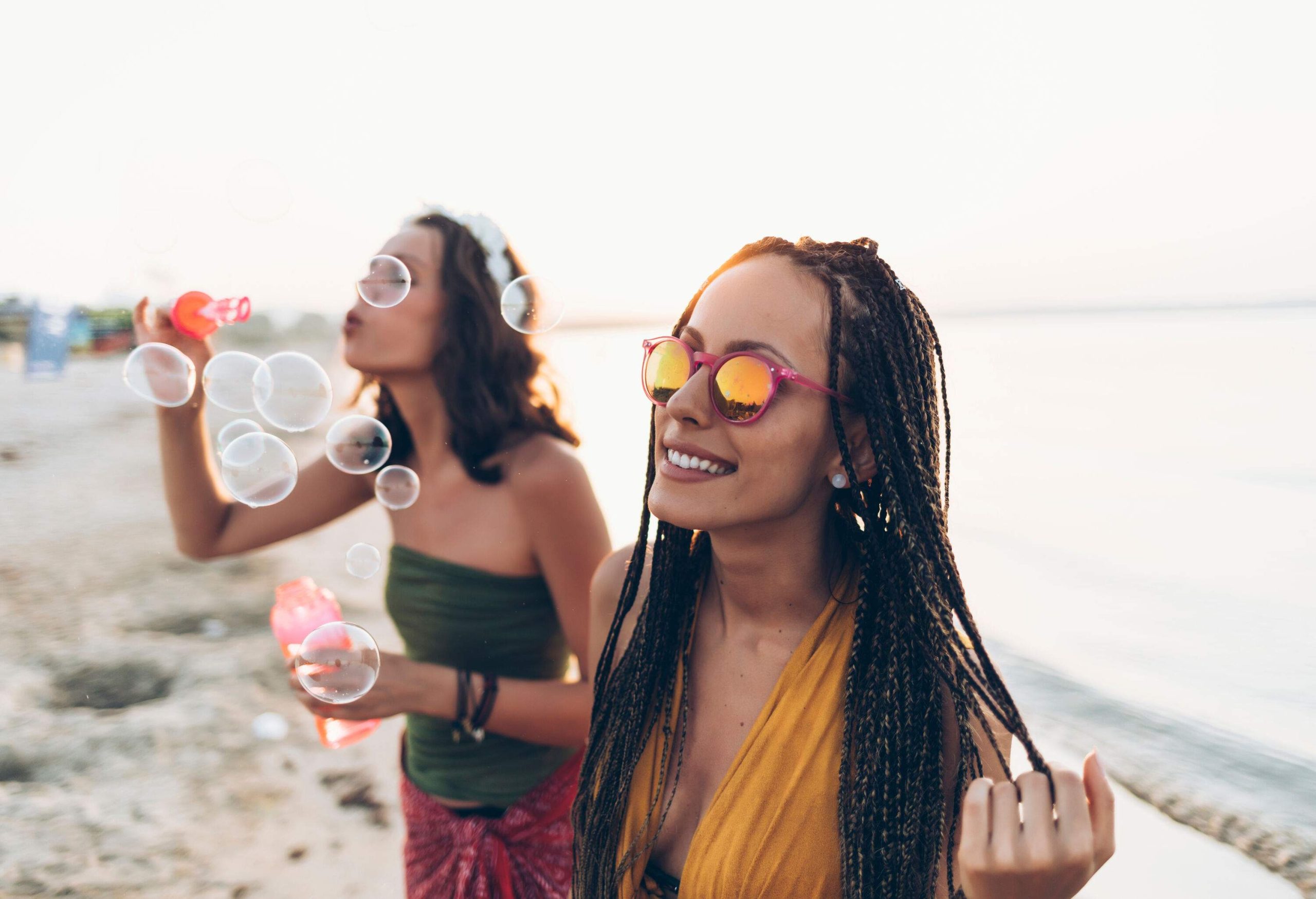 Young women on the beach, radiating joy and laughter, playfully blow bubbles.