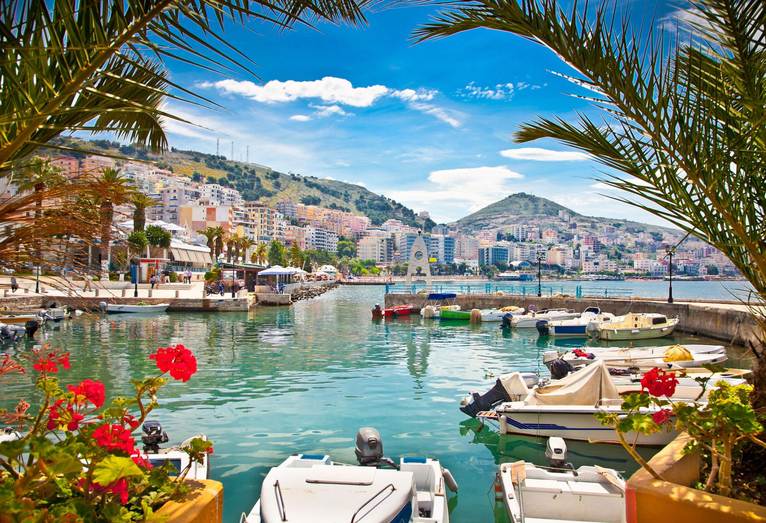 A coastal town with modern buildings on the foot of lush hills by the sea with moored boats.
