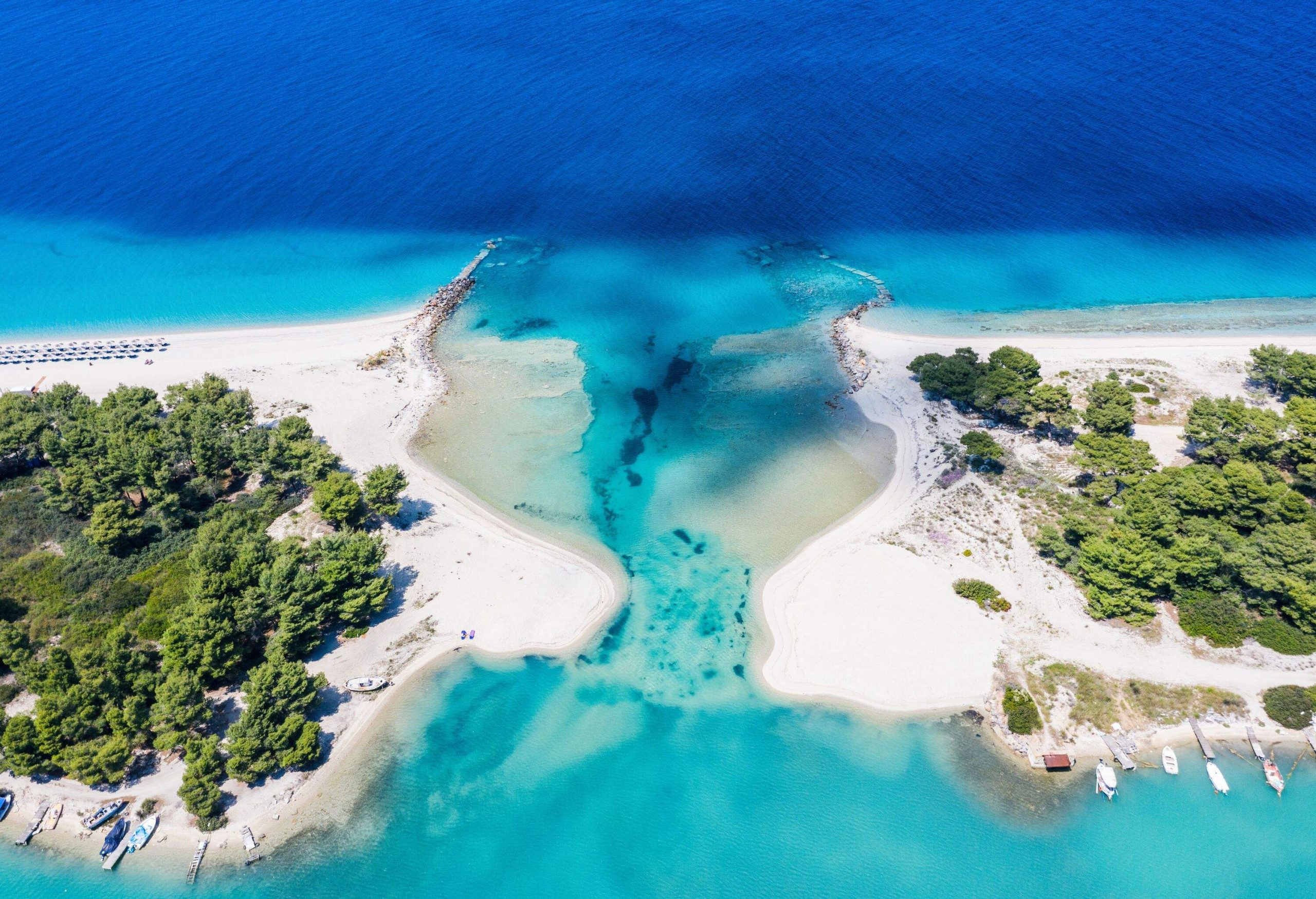 A white sand beach with an opening to a lagoon and port with anchored boats.