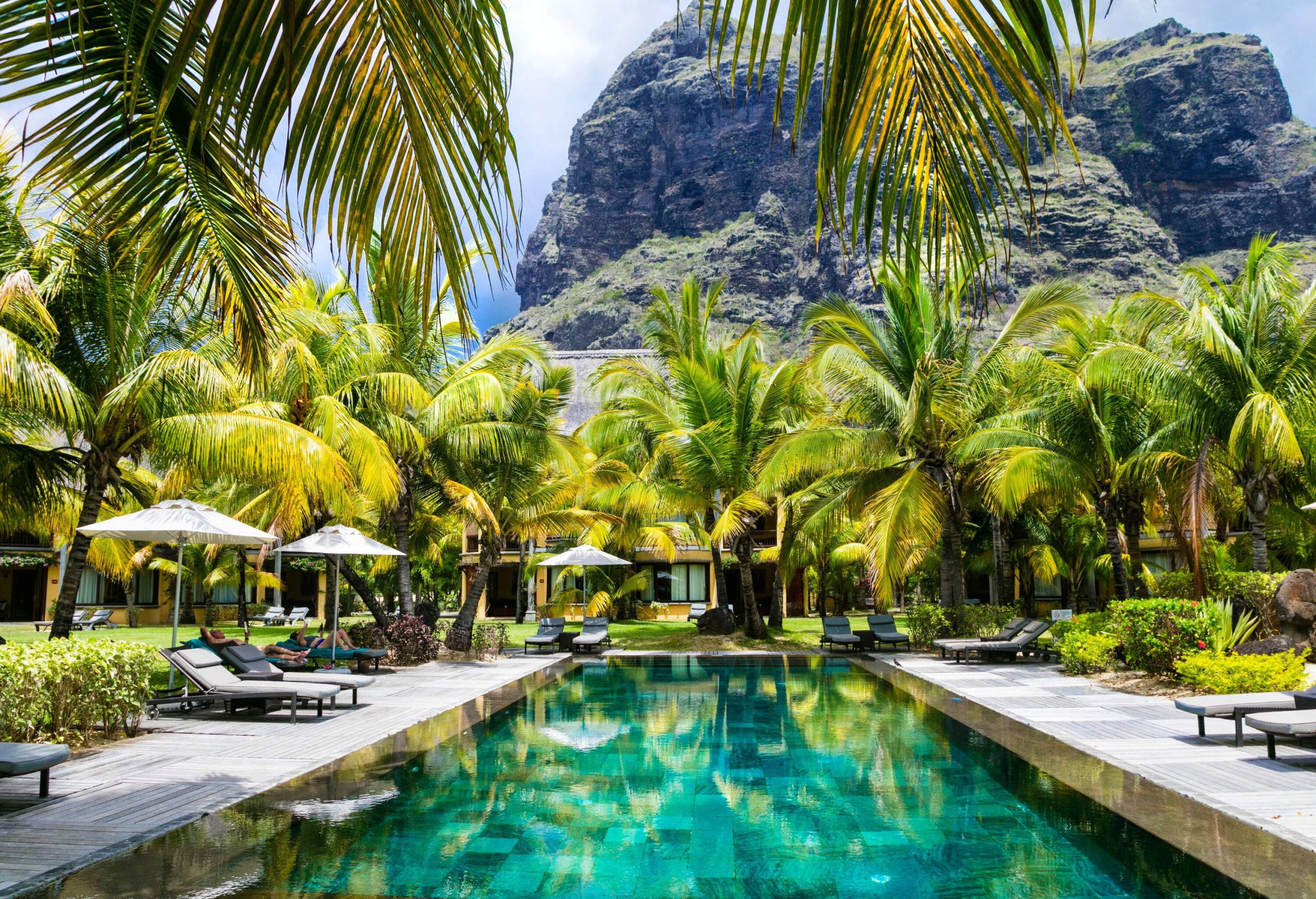 A luxury tropical resort with a spa swimming pool framed by palm trees with a rocky mountain in the background.