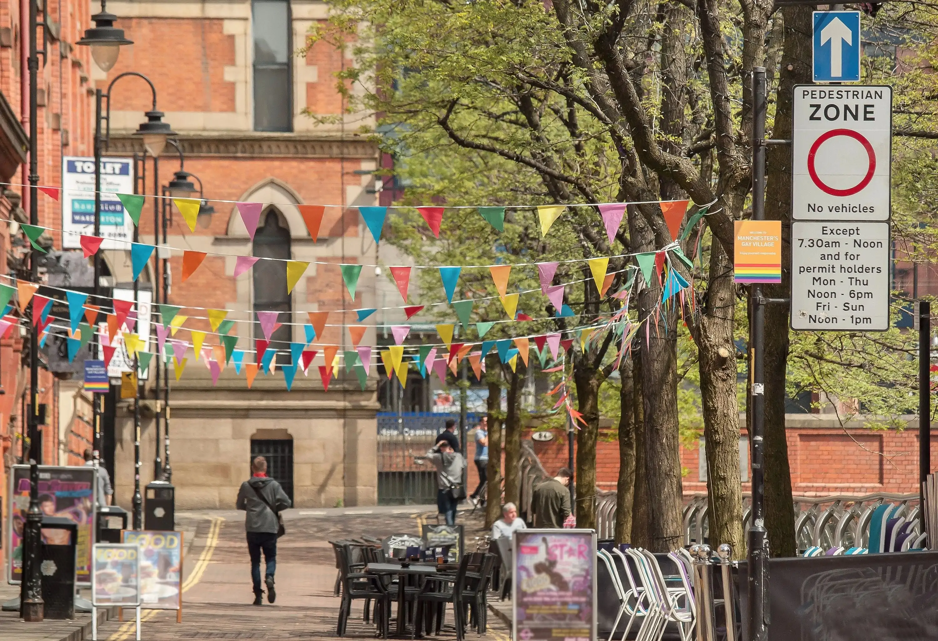A narrow cobbled street lined with traditional brick buildings with hanging colourful party flags.