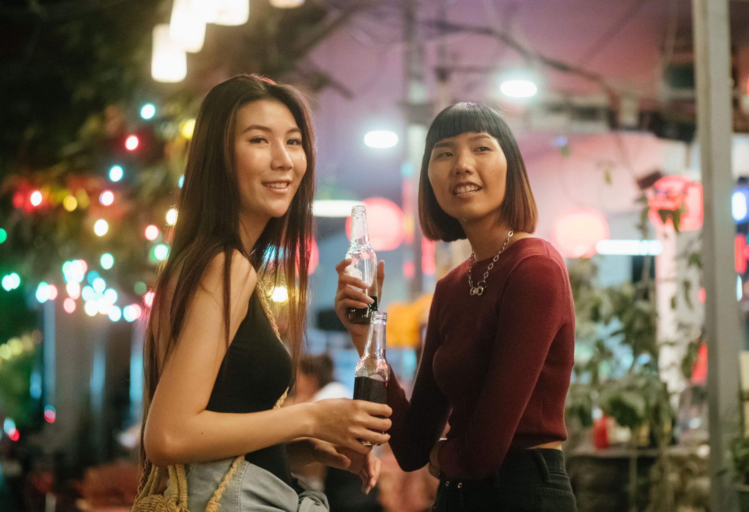 Two female friends enjoying a drink in a night market.