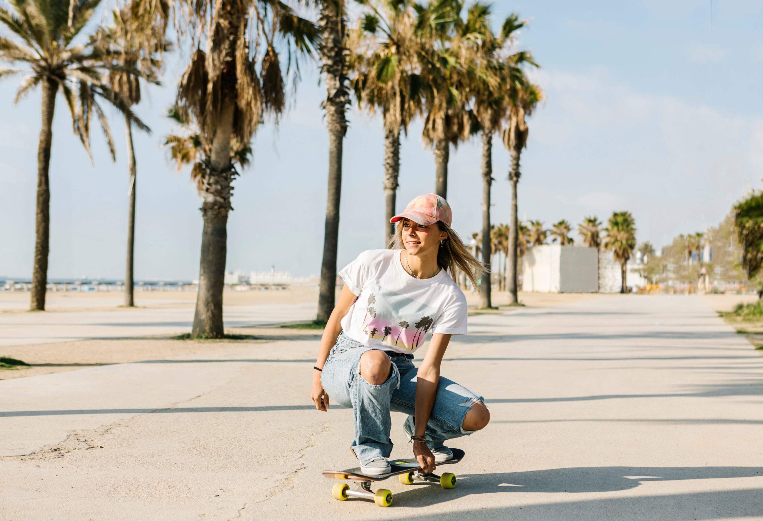 A female riding her skateboard on a paved road of the beach lined with tall trees.