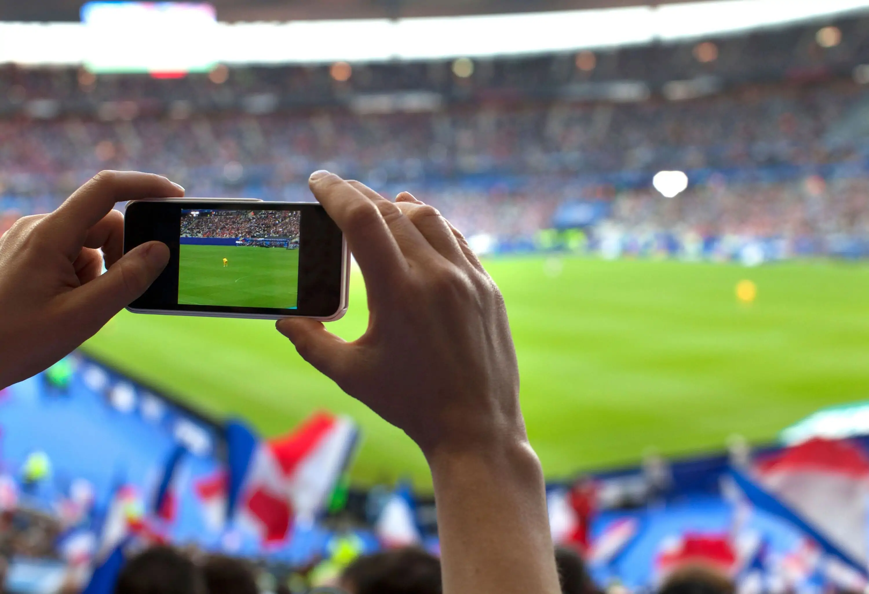 A person's hand using a phone to capture a memorable image of a bustling football stadium.