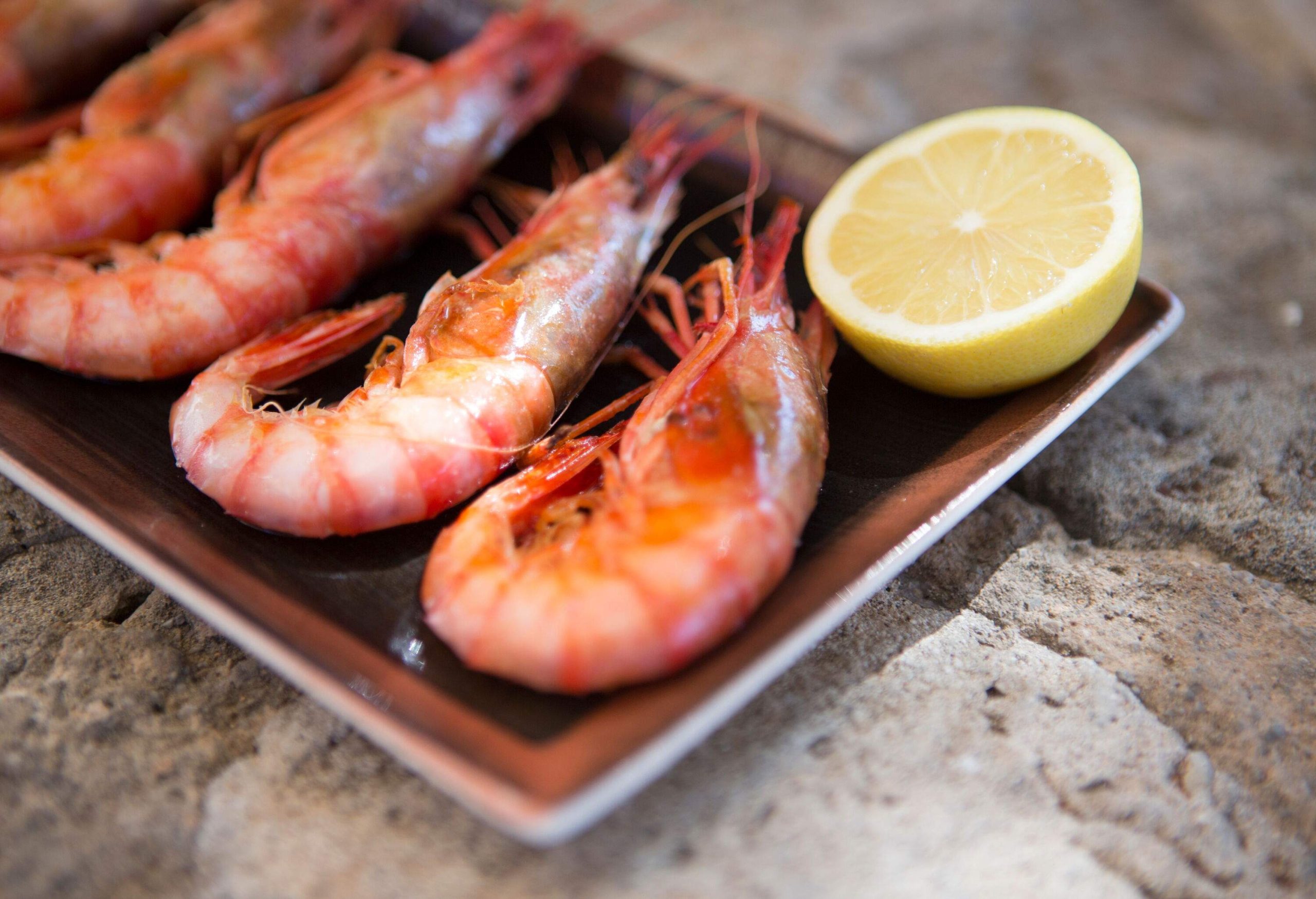 Steam shrimp and a slice of lemon placed on a wooden dish.