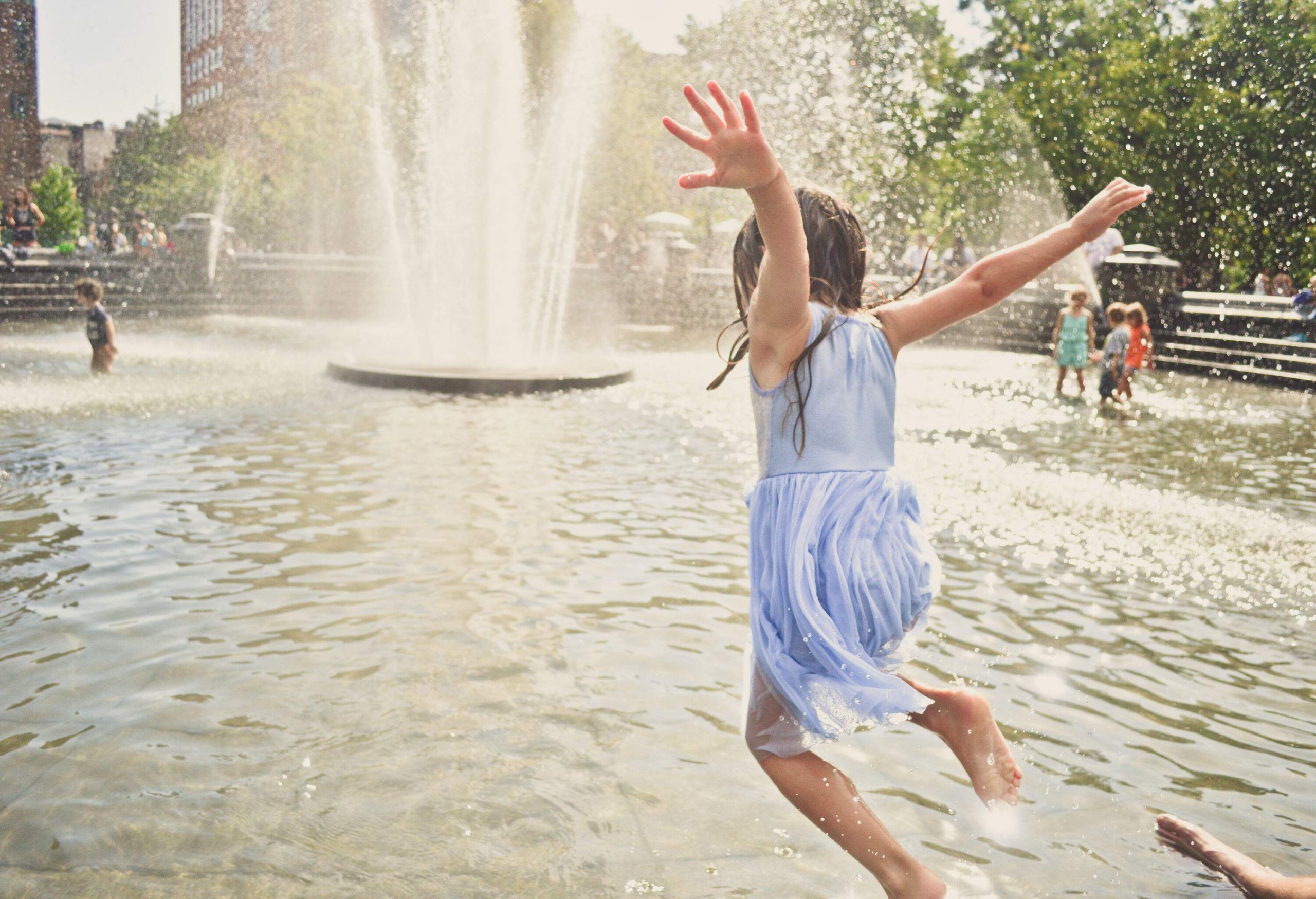 A young girl jumps into the water at a fountain on a hot summer day.