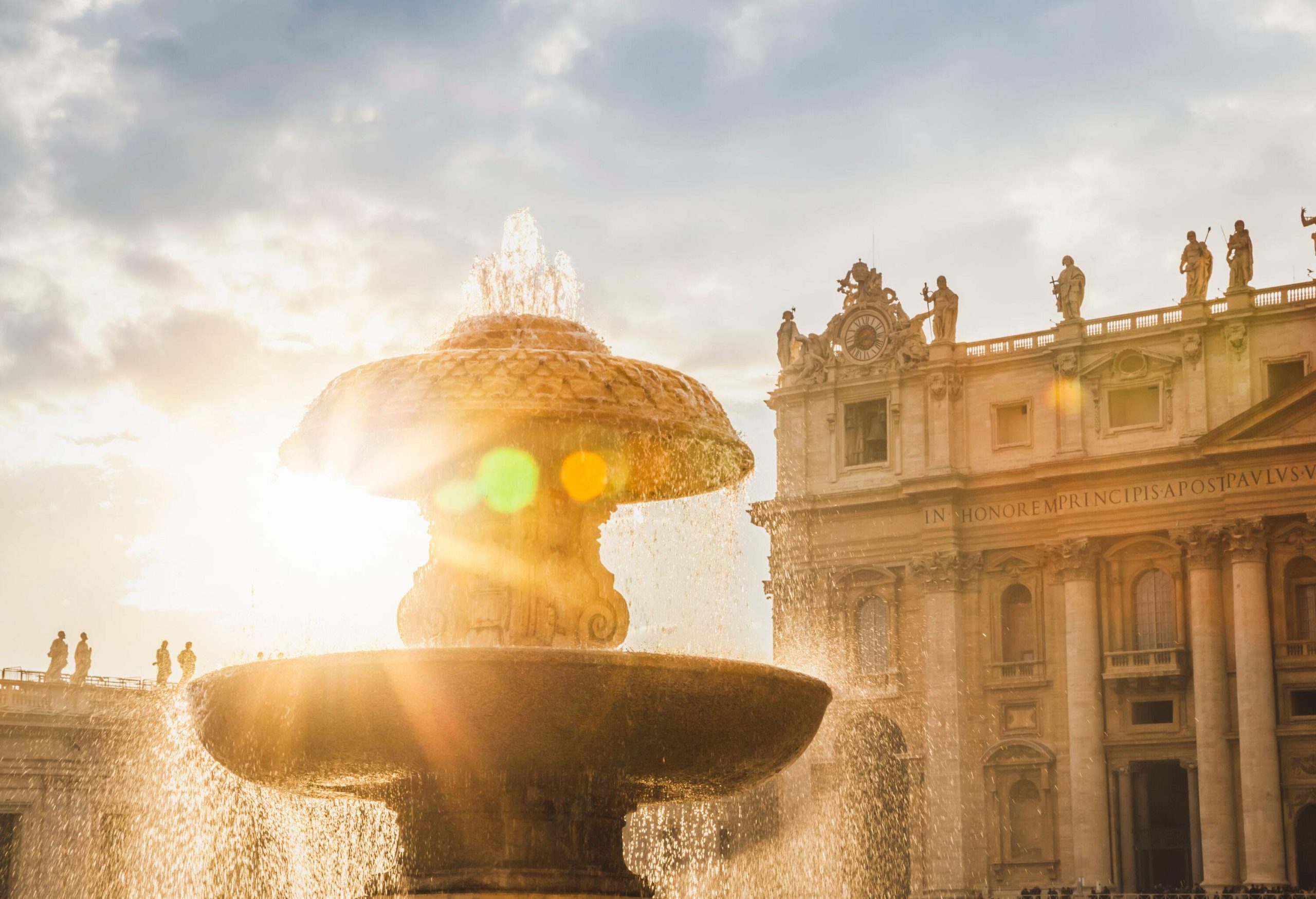The mesmerising sight of a stunning fountain set against a backdrop of ancient Roman structures, the brilliant sun illuminating the cascading water as it splashes playfully in the air.