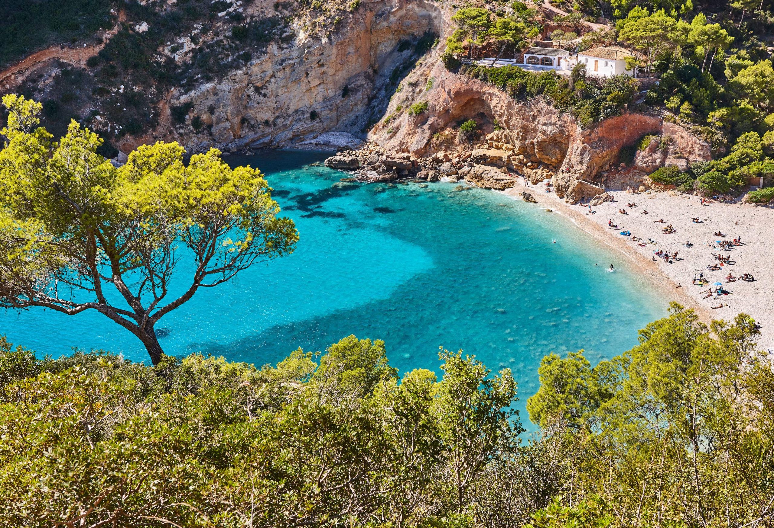 People lounging on the beach of a cove surrounded by rock cliffs.