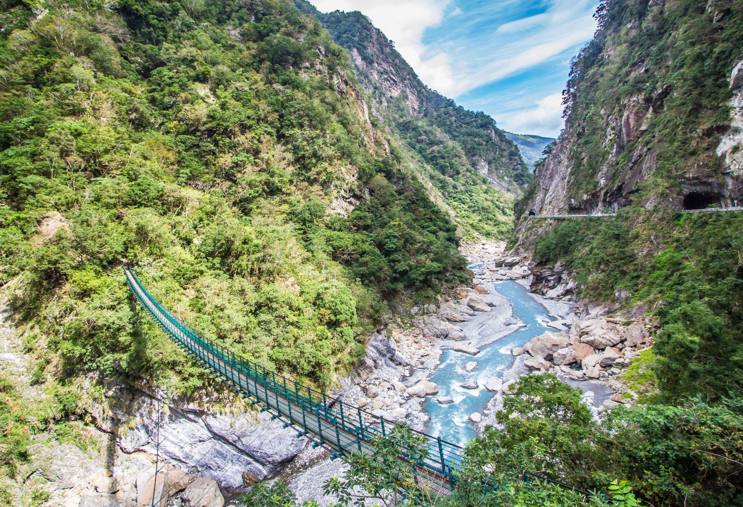 A river gushes between the deep gorges, spanned by a narrow green footbridge.