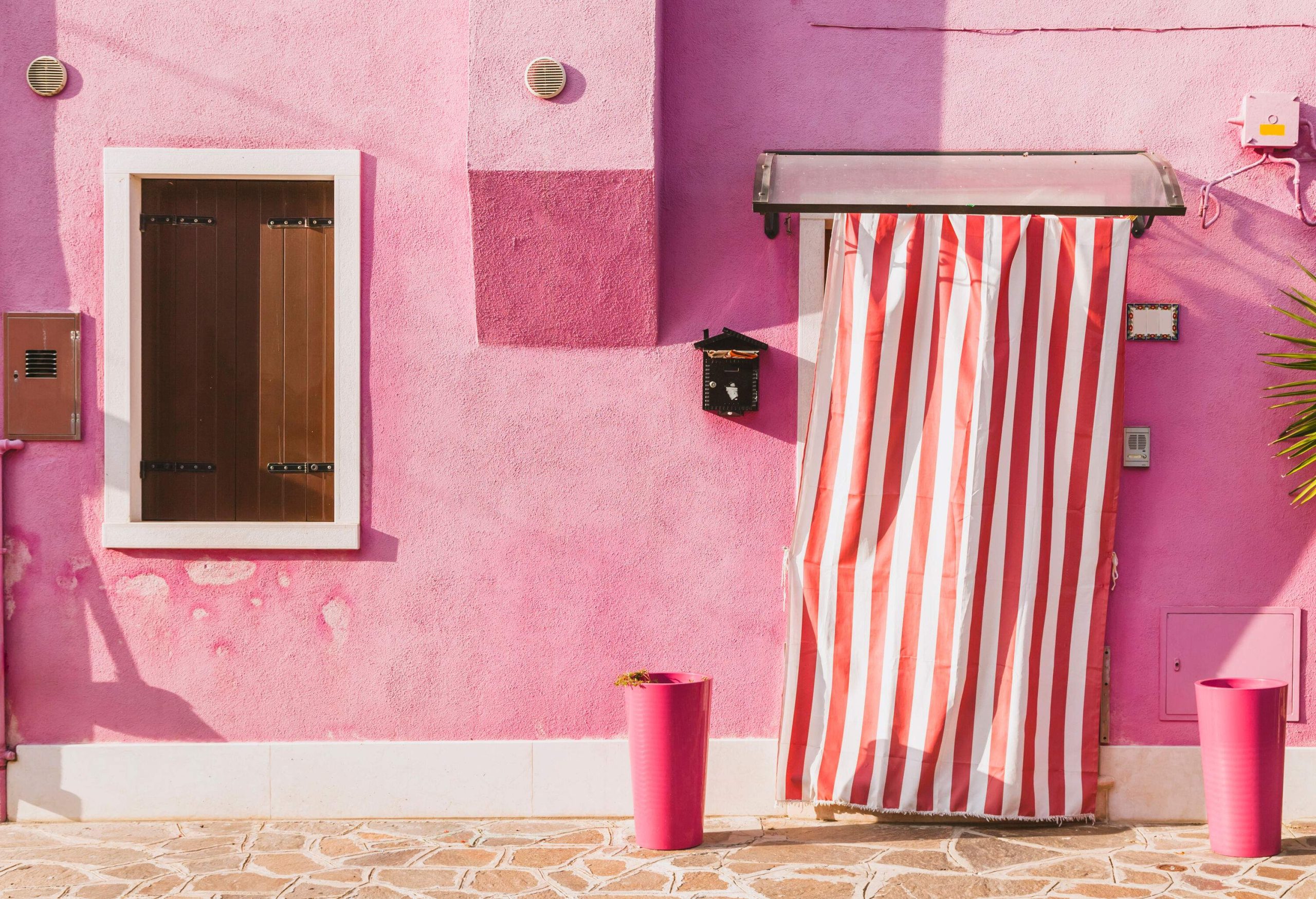 A pink stucco structure with a white-trimmed window and a red and white striped door cover.