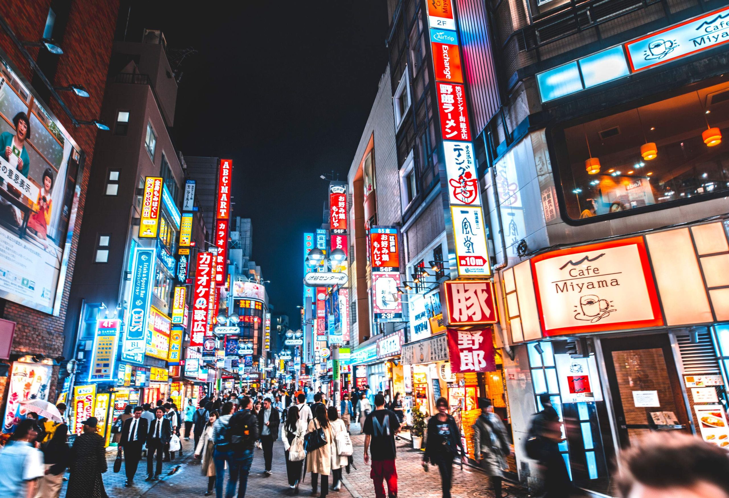 A nighttime scene in one of Shibuya's bustling districts flanked by shops and cafes.