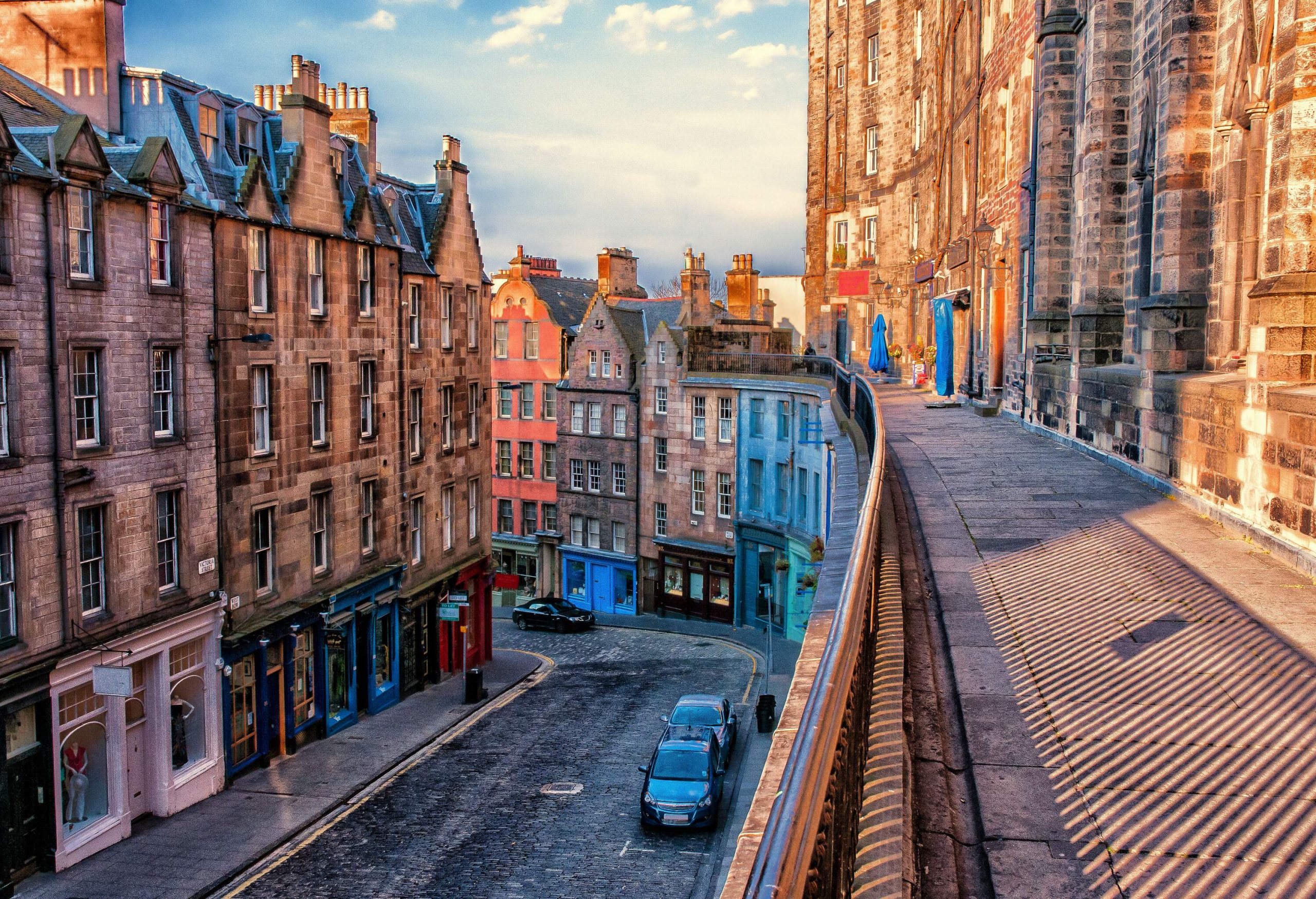 A terrace running above a steep street lined with old town buildings and colourful shopfronts.