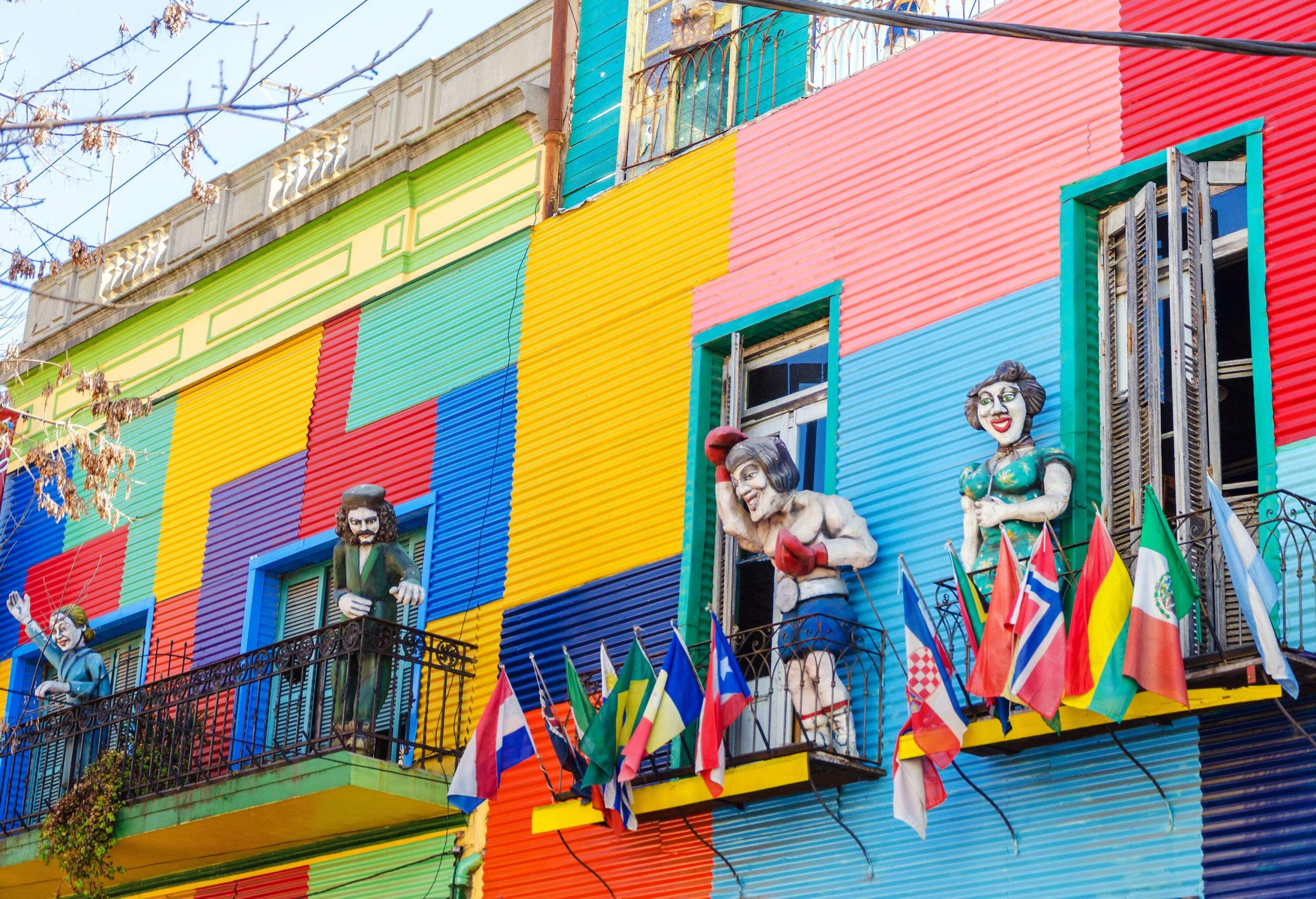 A building with colourful walls with human statues and country flags on its balconies.