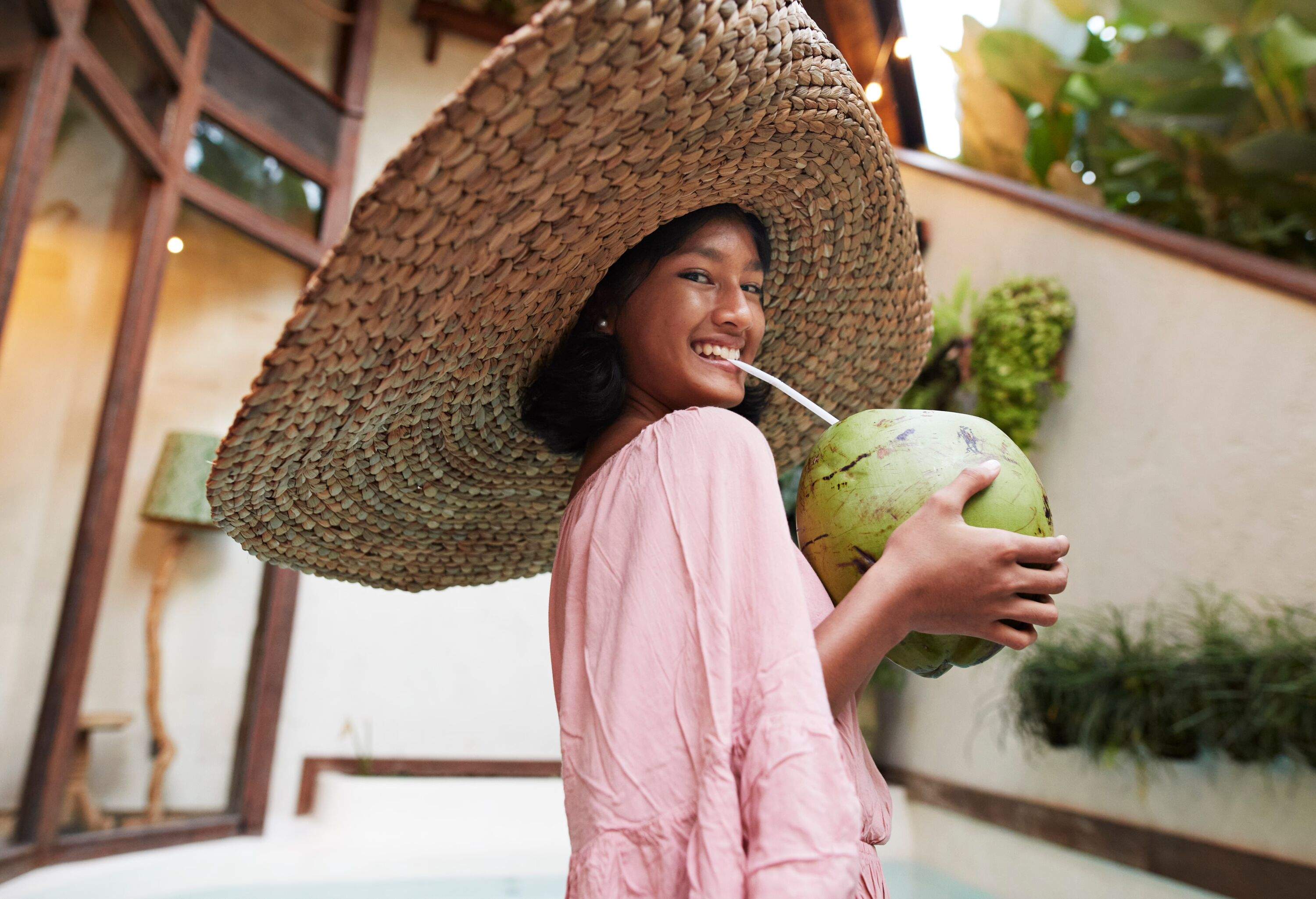 Portrait of happy girl wearing large straw hat and drinking coconut water during vacation