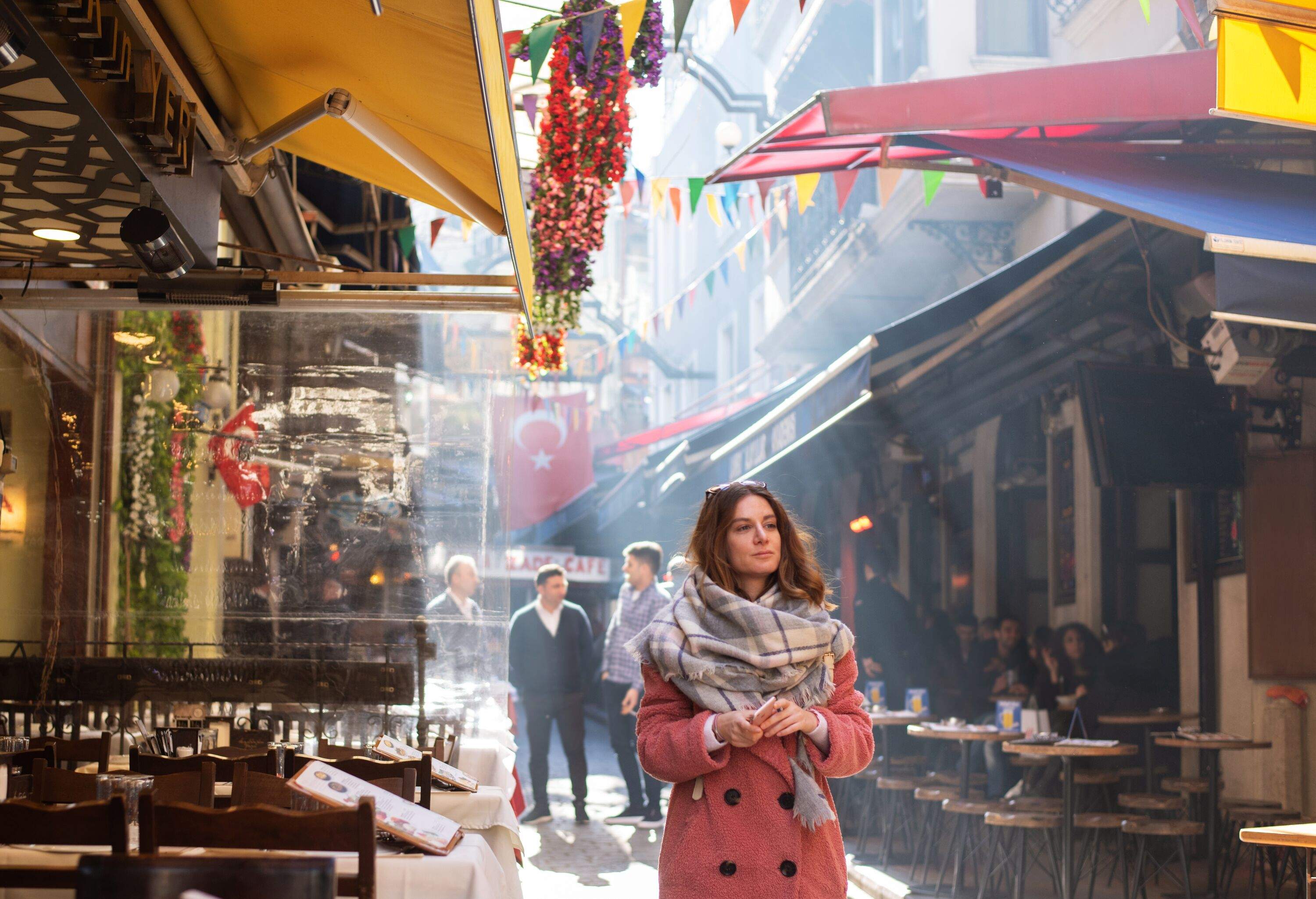A woman in a coat and scurf strolls past a row of eateries as smoke drifts in the distance.