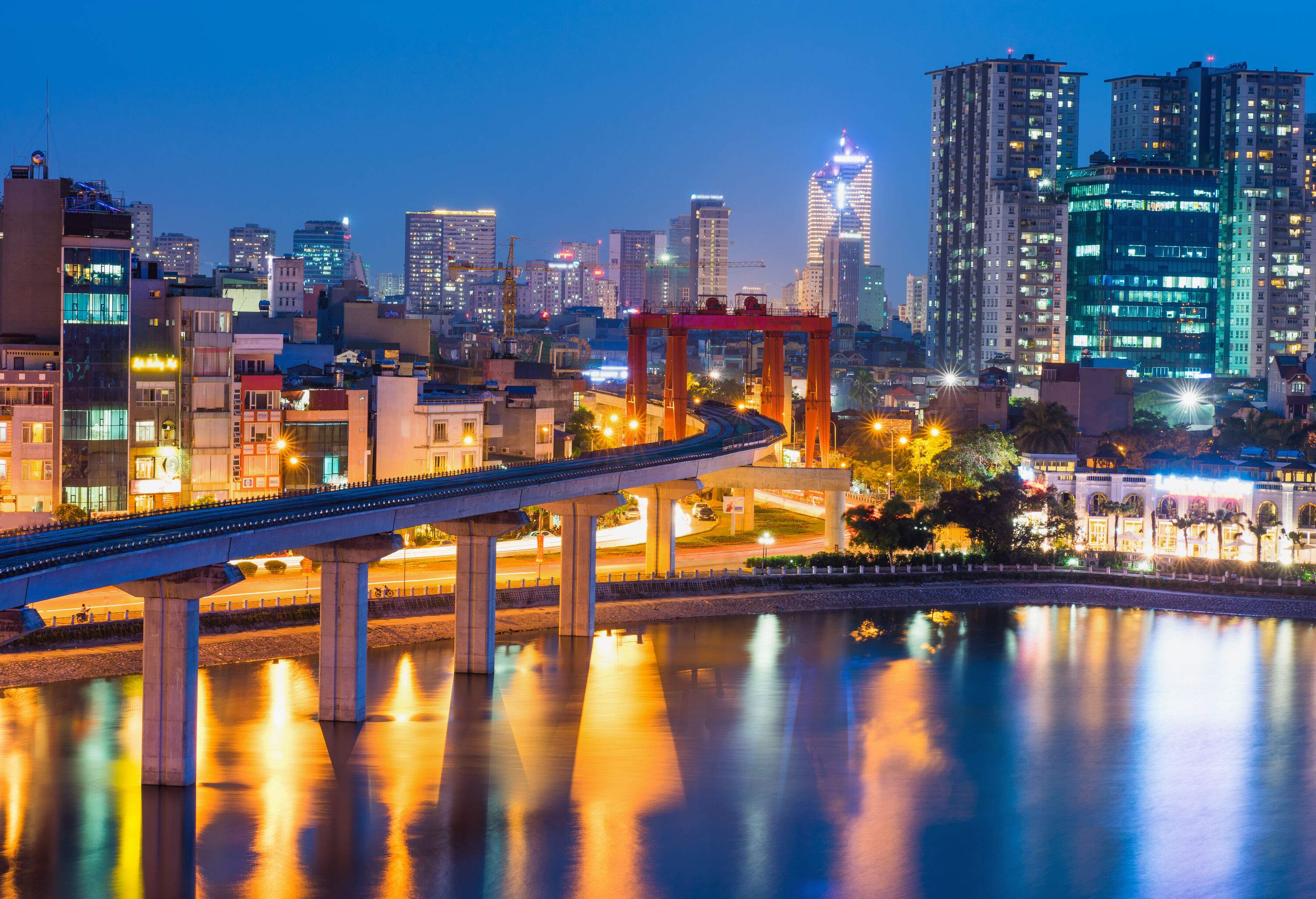 A railway bridge across a lake with night-time views of the metropolitan skyline.