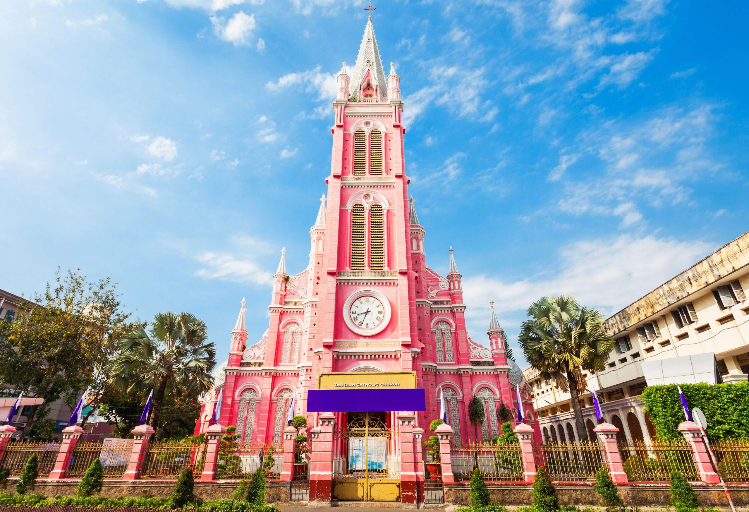 A remarkable pastel pink church with a central clock tower between the buildings.