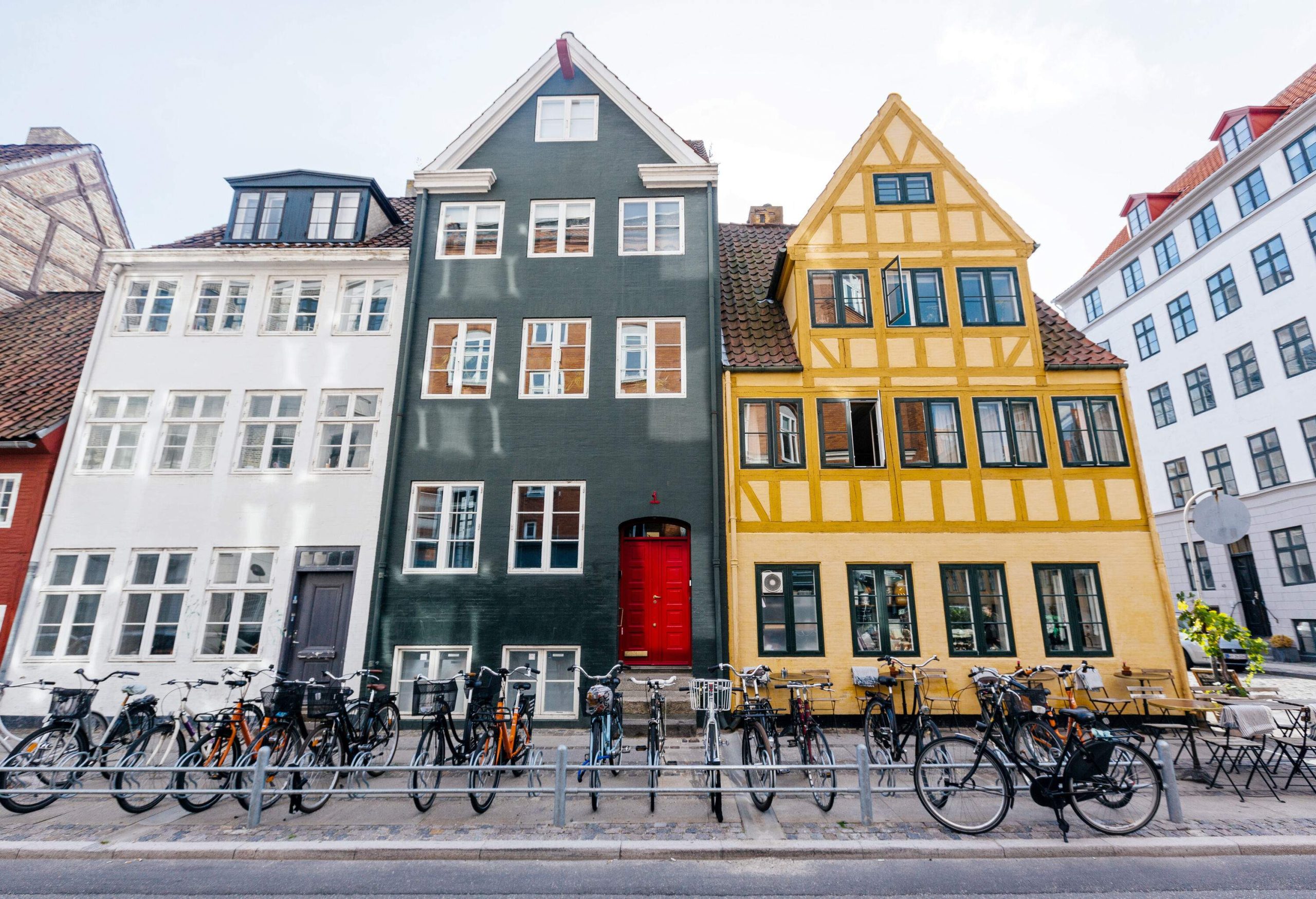 Bicycles lined up along the curb in front of a row of multi-story, multi-coloured buildings.