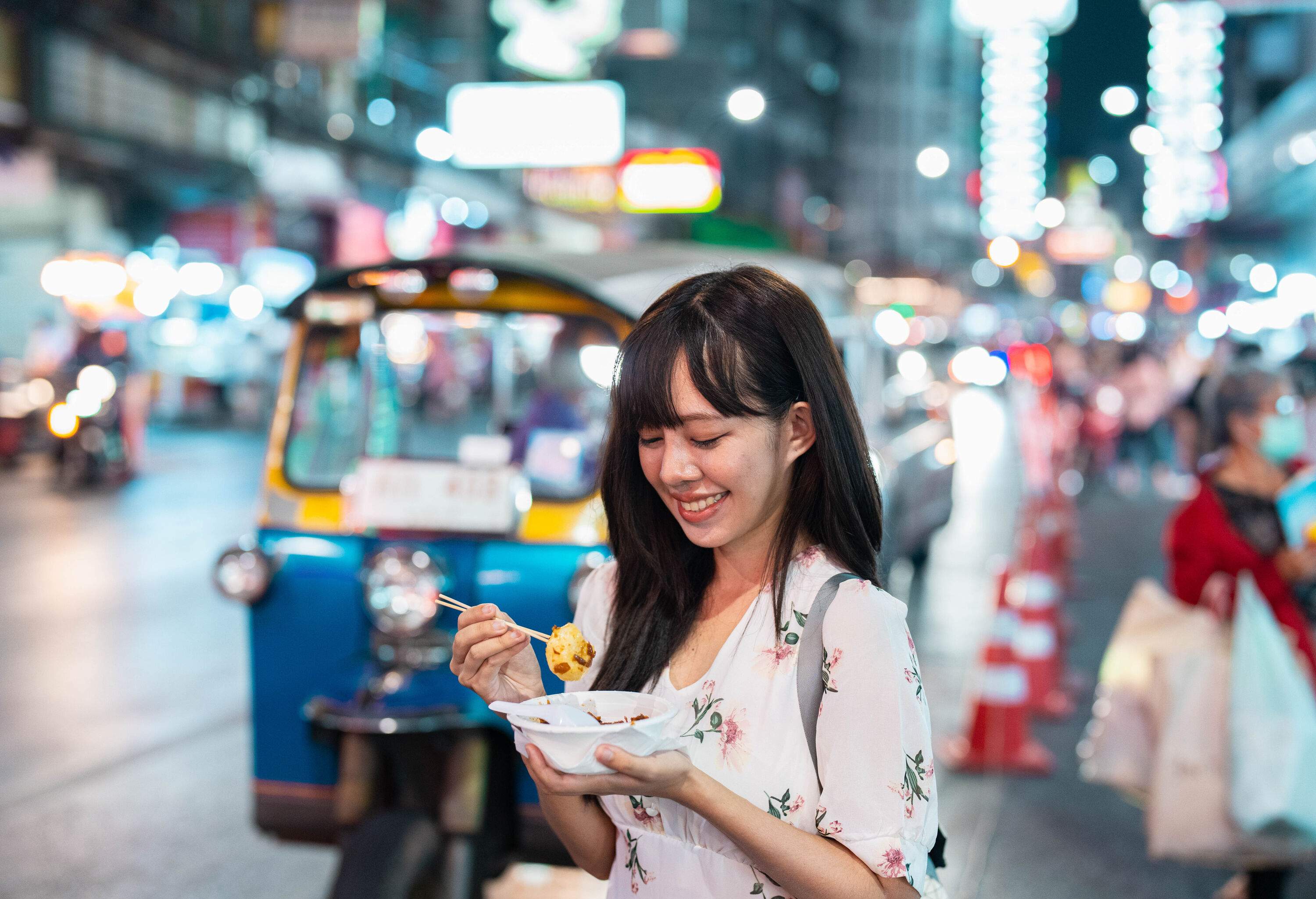 A young woman holding a bowl of street food at a night market.