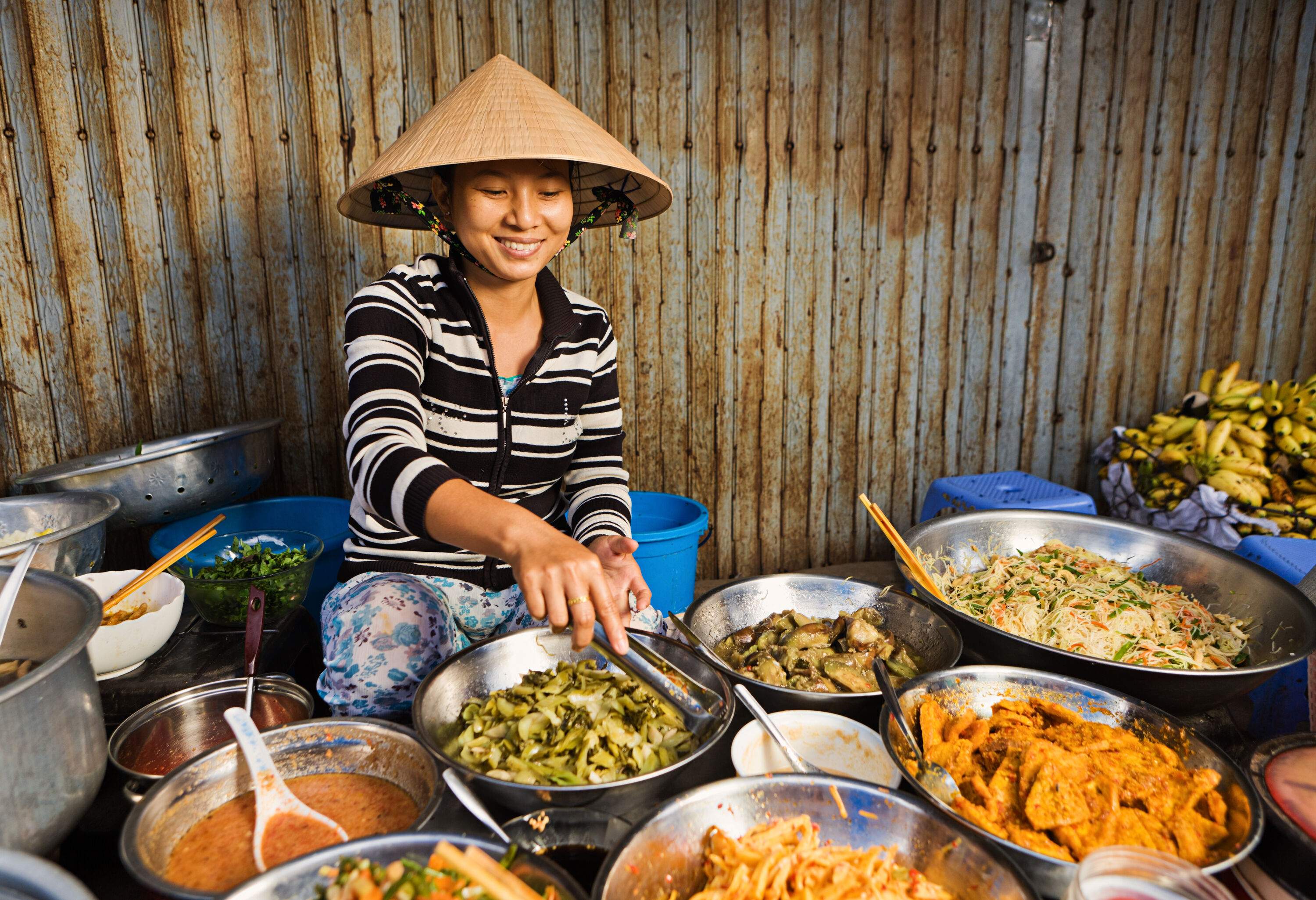 A woman in a straw hat sells a variety of food in the street.