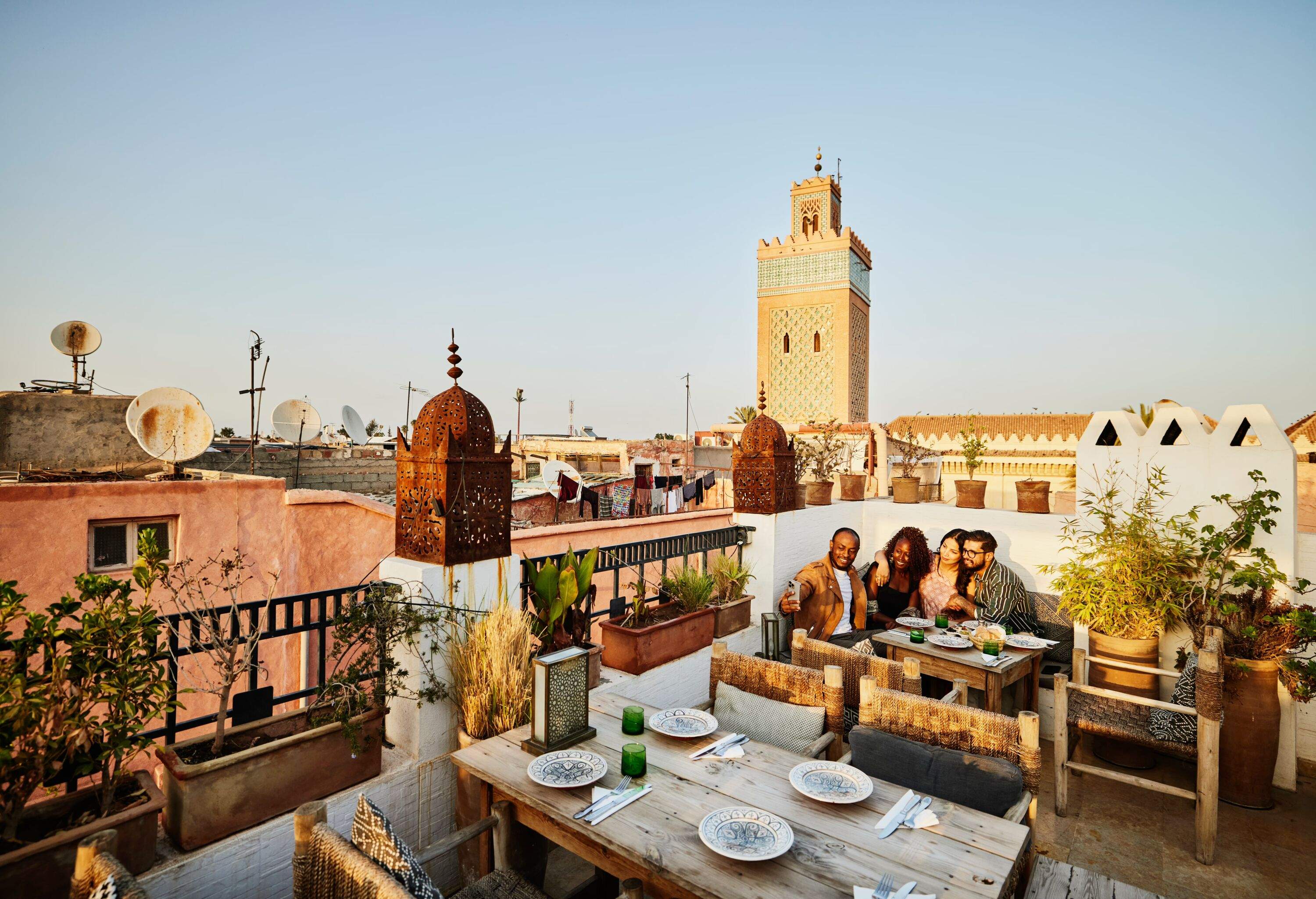 Wide shot of smiling couple taking selfie while dining with friends at rooftop restaurant in the Medina of Marrakech while on vacation