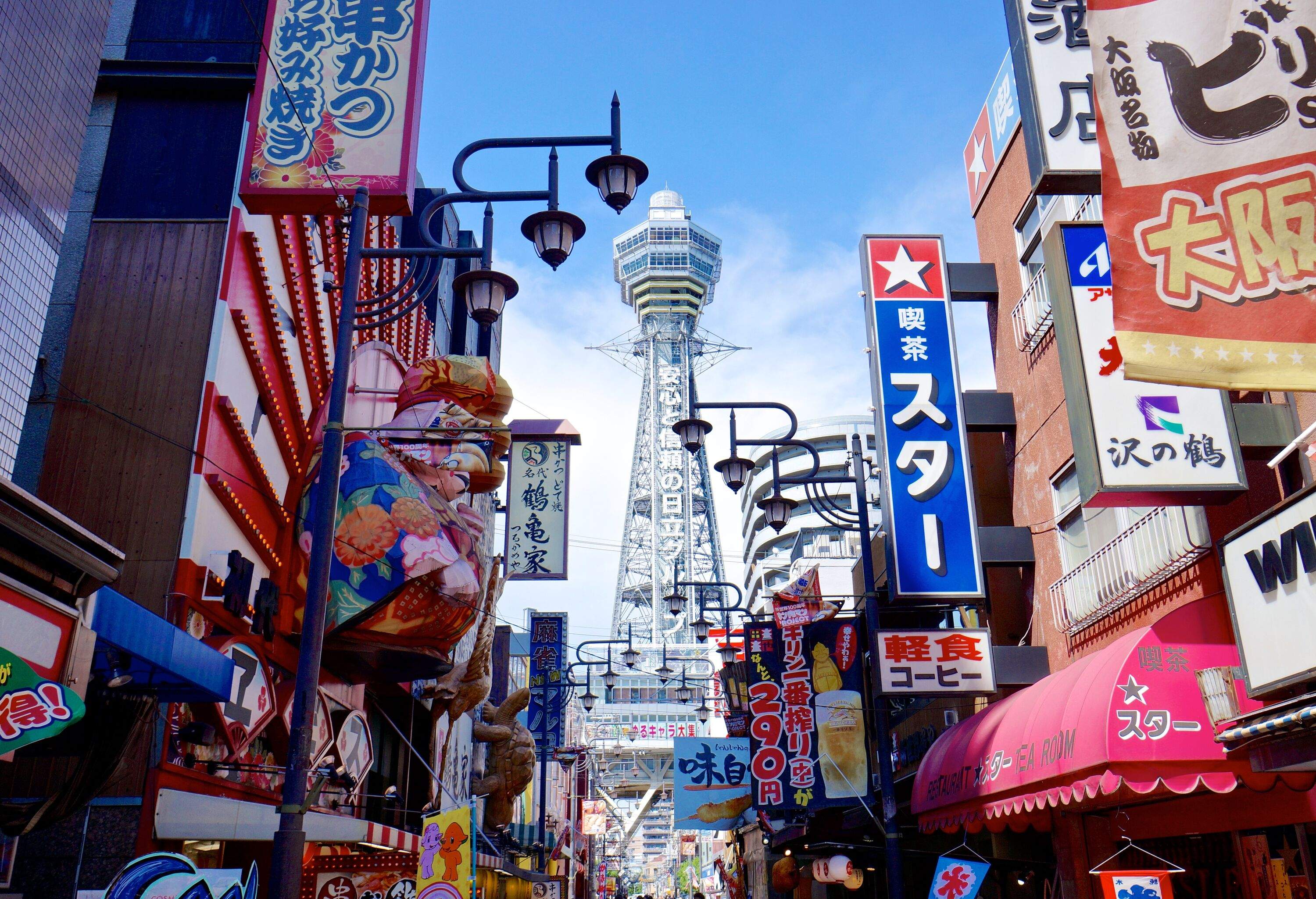 A row of commercial establishments with colourful advertisement signages against the backdrop of an observation tower.