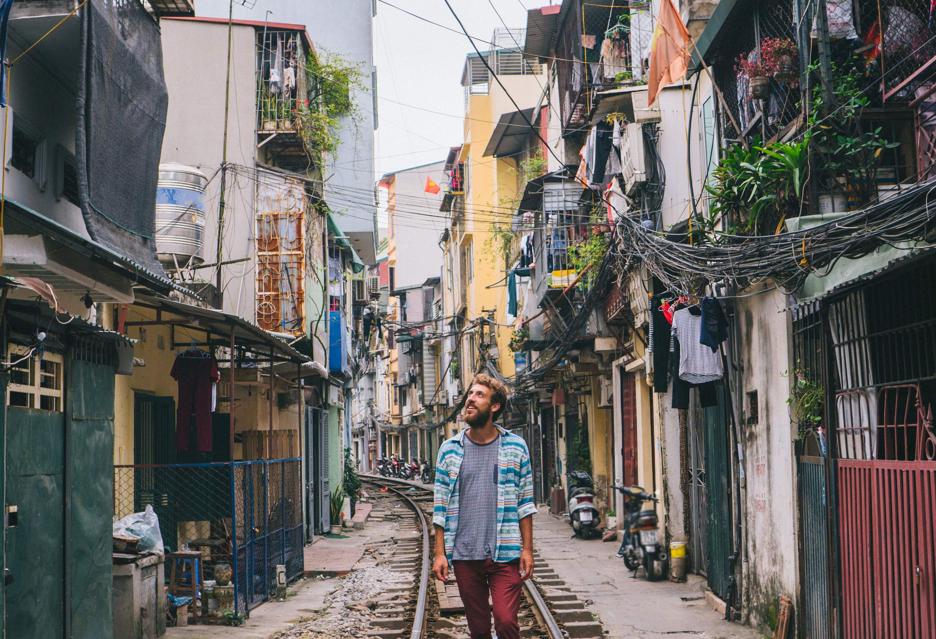 A man in casual clothes stands on a railway bordered by residential buildings.