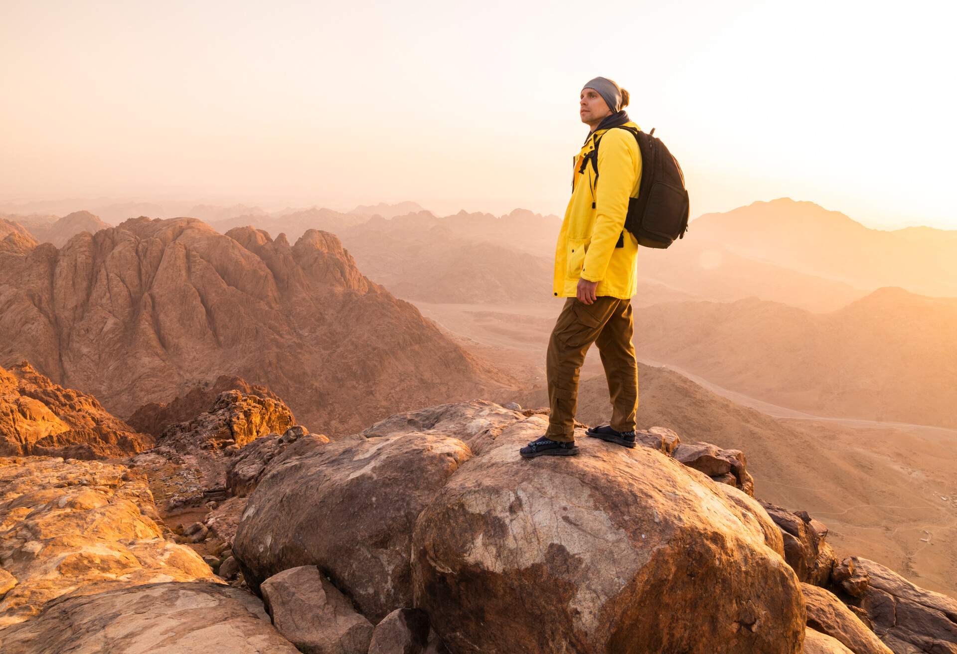 A male hiker stands tall on a rock boulder atop Mount Sinai.